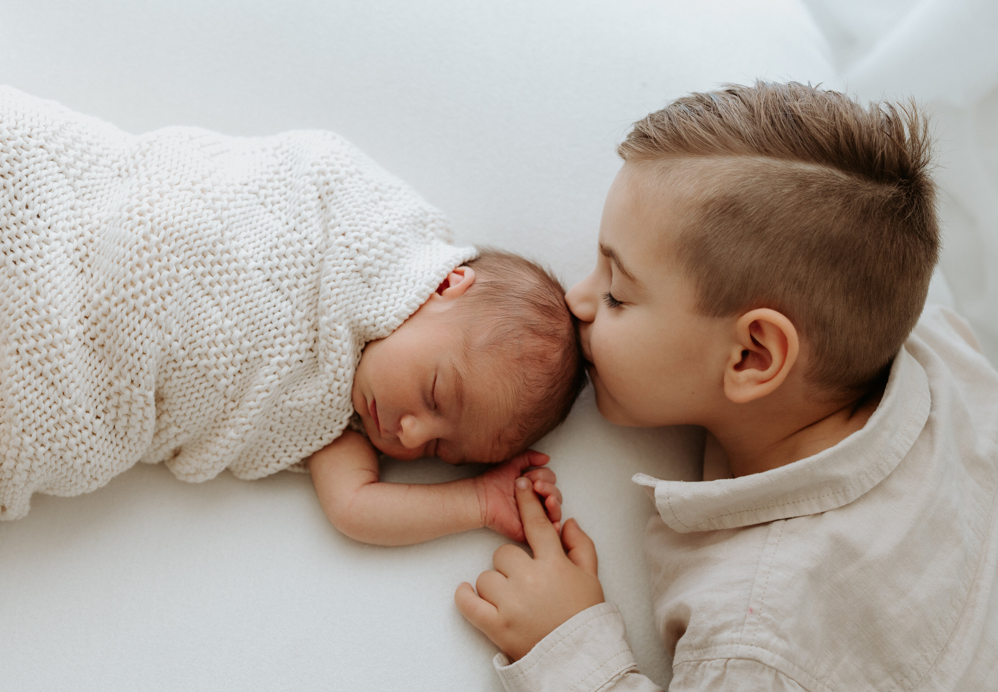 brother kissing baby on forehead during indoor newborn photography session in perth