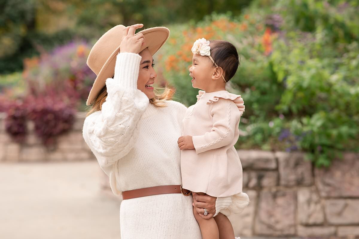 Mom in cream dress with a hat making young daughter smile for Maryland Family Photos