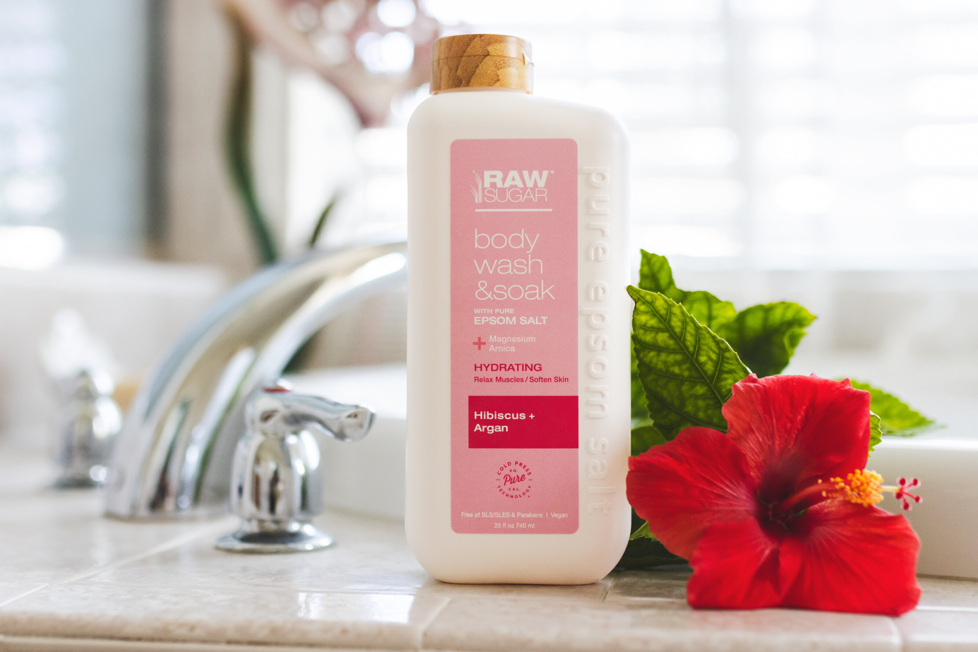 Beauty product photo of Raw Sugar hibiscus body wash in a bathtub with a hibiscus flower