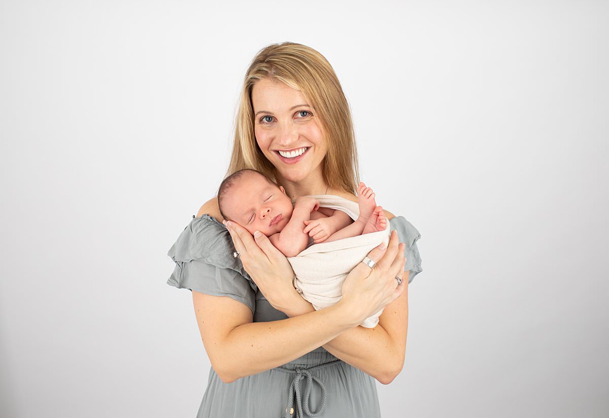 Mom in teal dress holding new baby in studio by Columbia MD newborn photographer