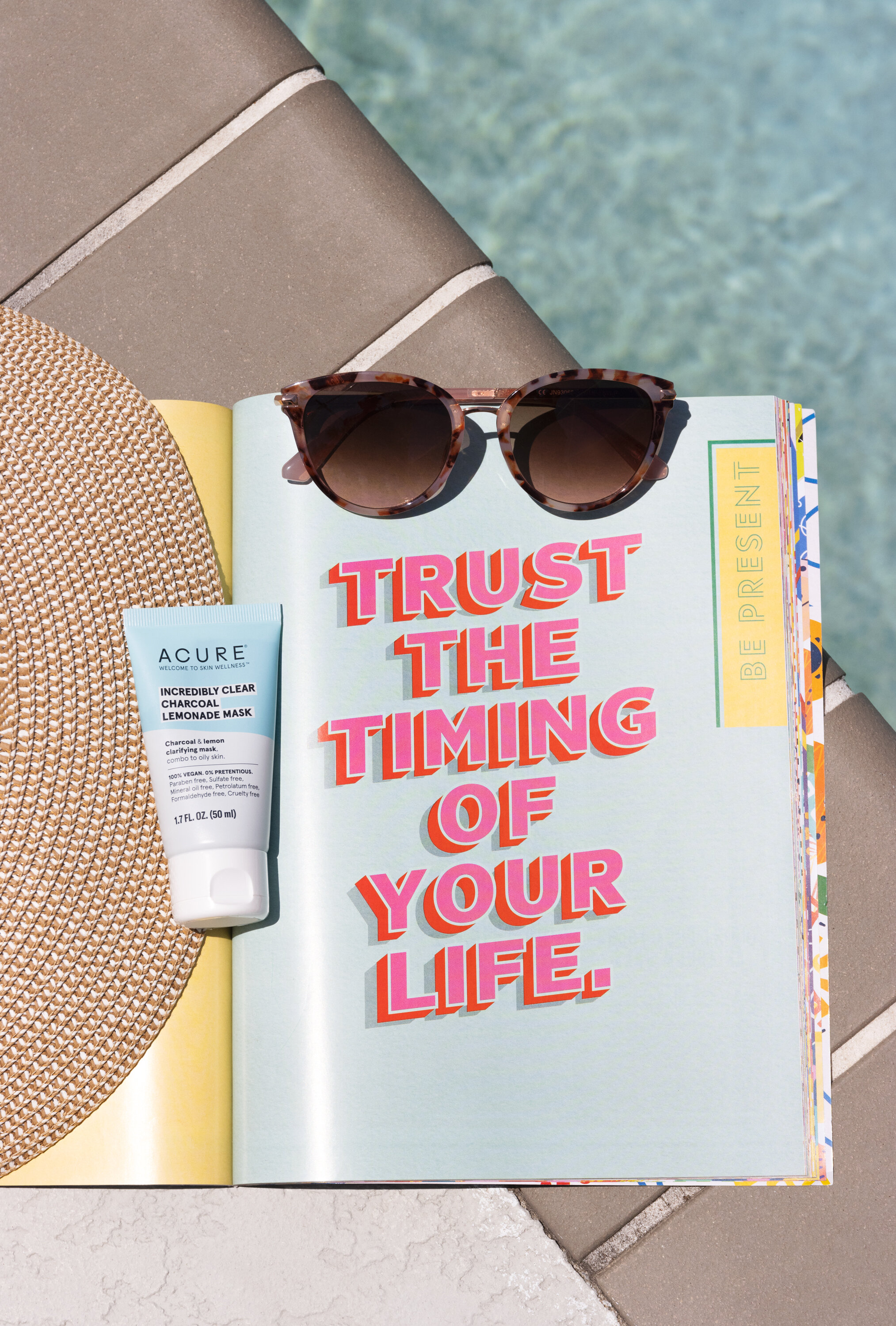Flatlay of skincare products arranged on a magazine with motivational quote beside a pool
