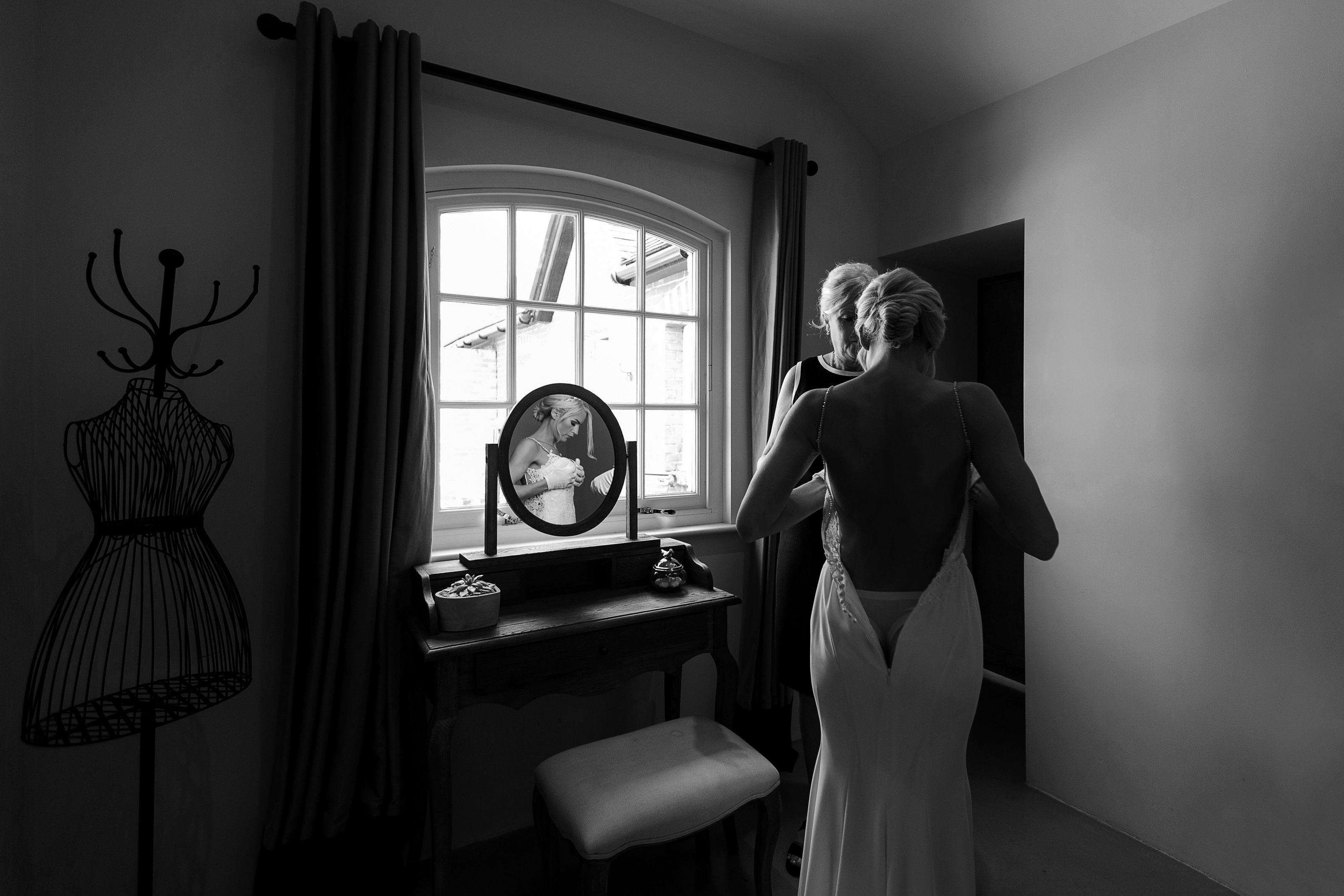 Stunning natural light black and white wedding photography by Adorlee of this beautiful bride getting ready for her wedding and doing up her Enzoani gown and reflection in the dressing table mirror