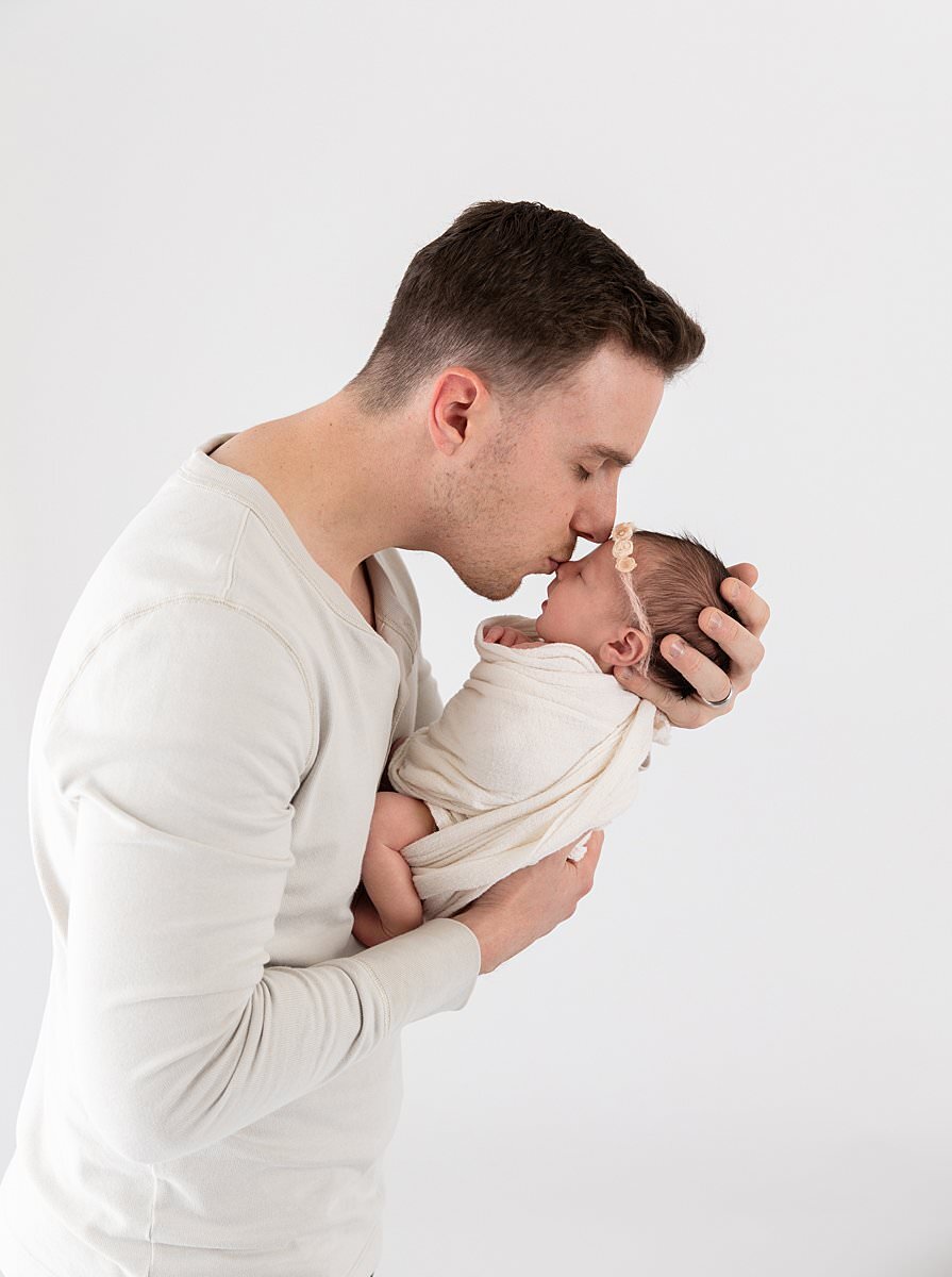 Dad holding baby kissing her forehead by Columbia MD newborn photographer