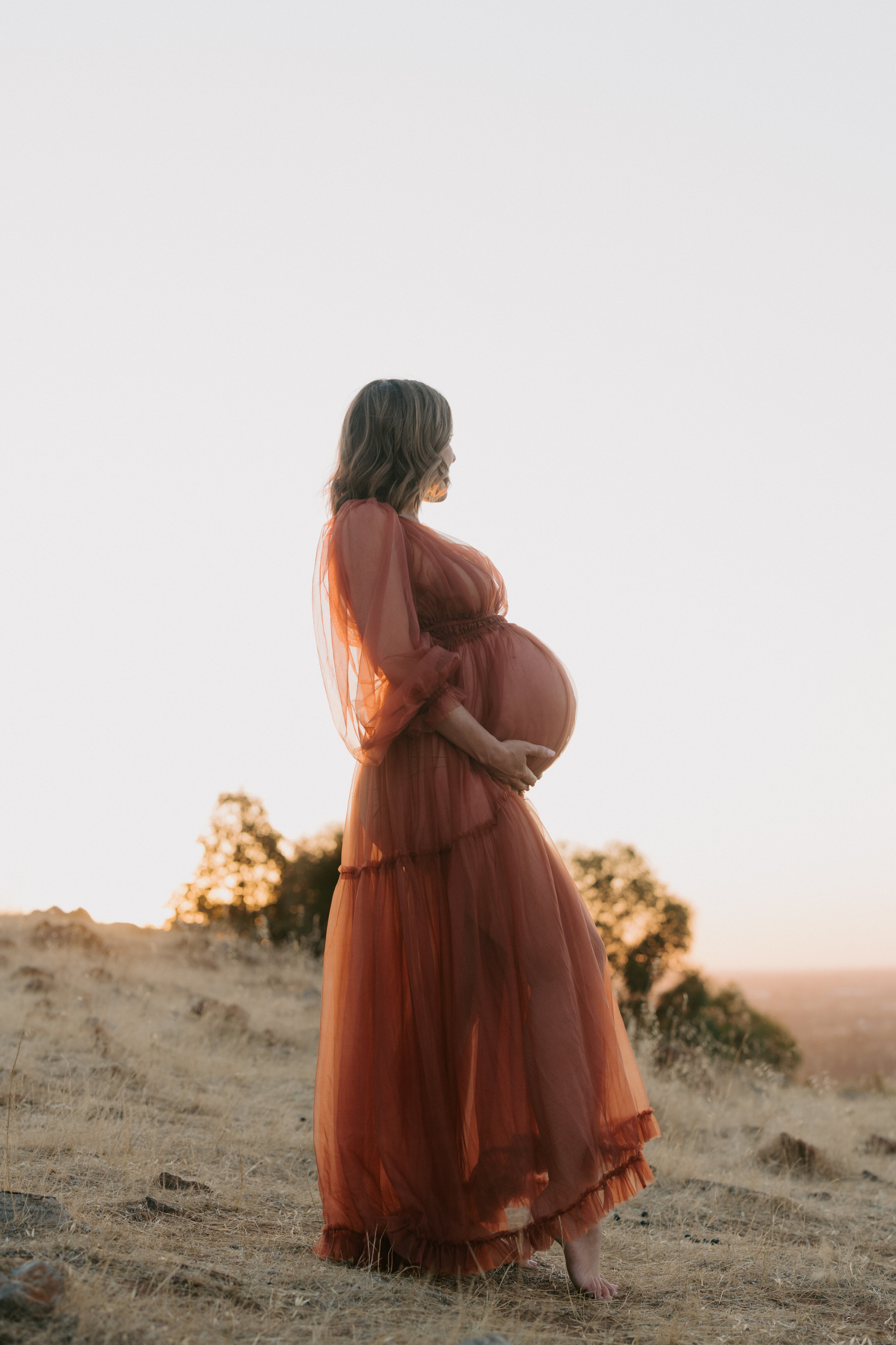Glowing mother-to-be embracing her baby bump during golden hour in Perth
