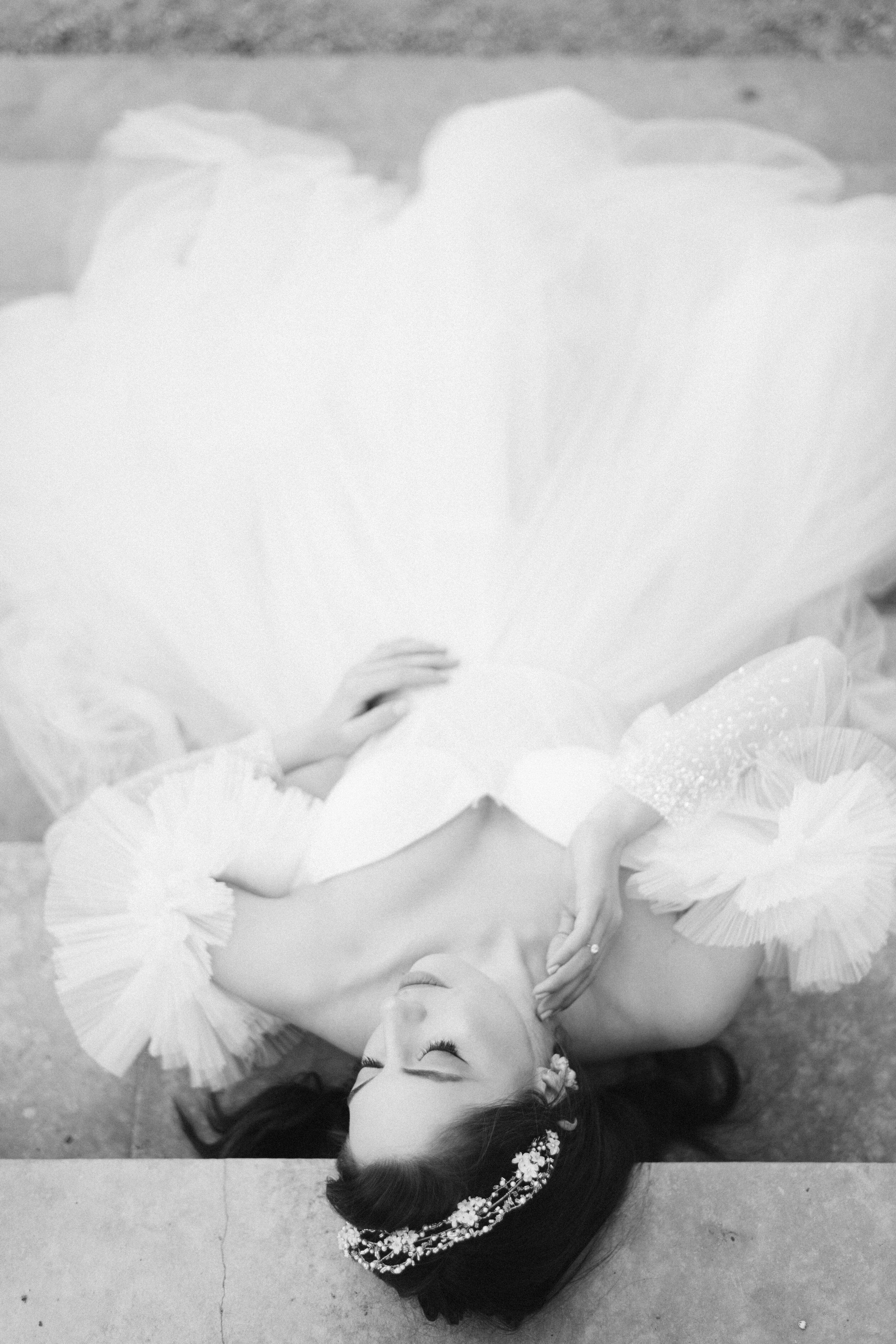 Bride in layered tulle gown lying on stone steps in Italy with eyes closed — romantic and editorial.