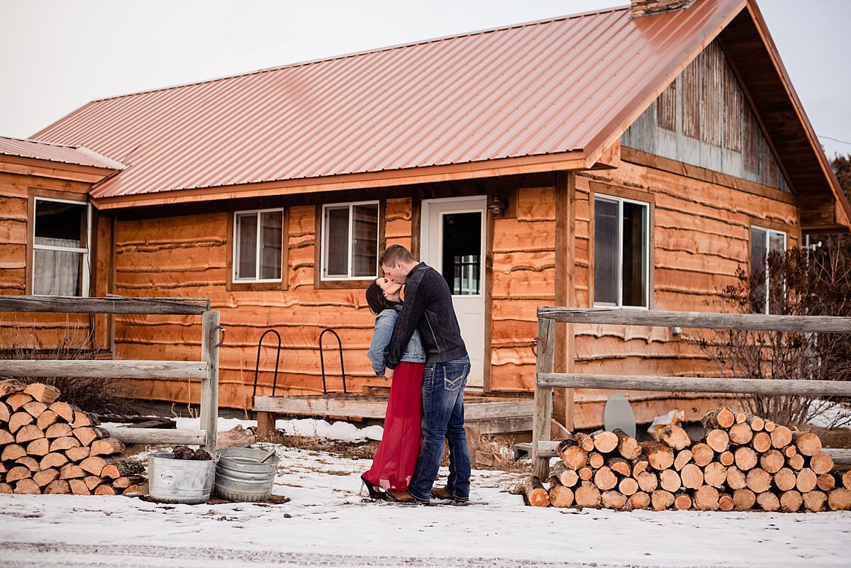 Couple kissing outside log cabin in snow outside Bozeman Montana