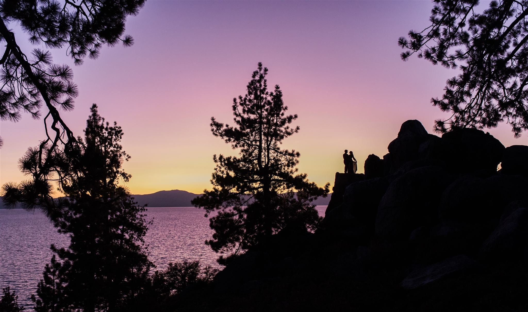 silhouette photo of couple suring sunset on the rocks by lake tahoe