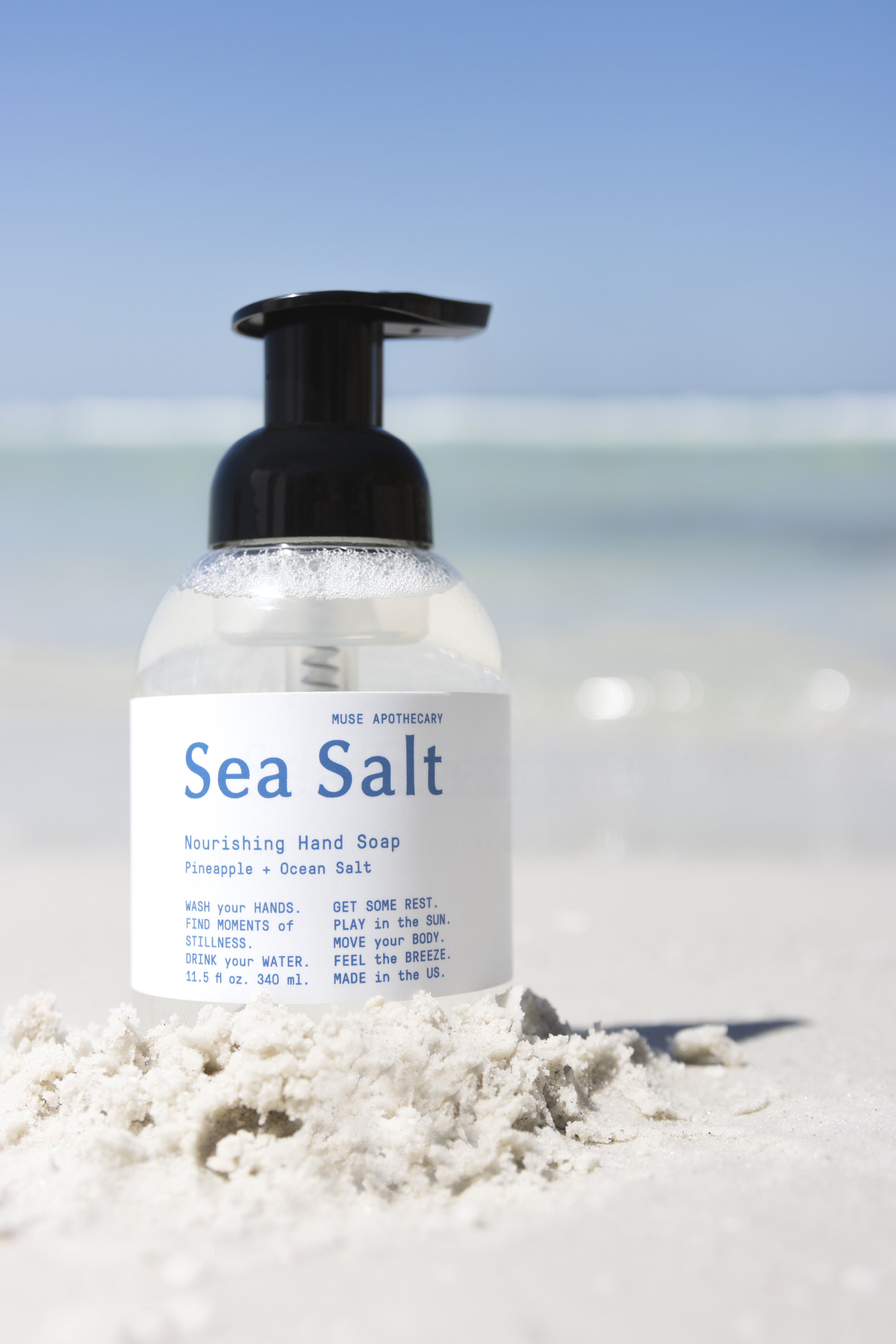Sea salt hand soap photographed in natural light placed in the sand with the ocean as the background