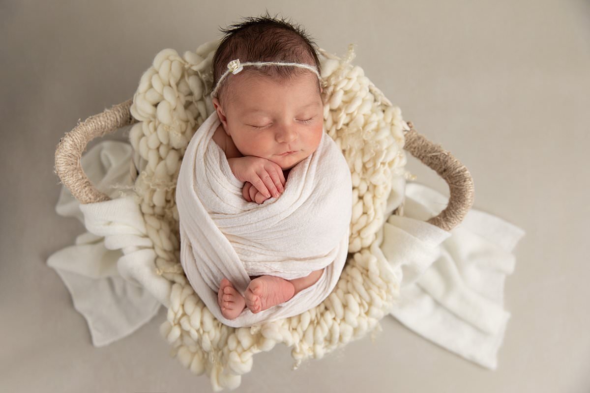 Swaddled baby girl in cream blankets in basket