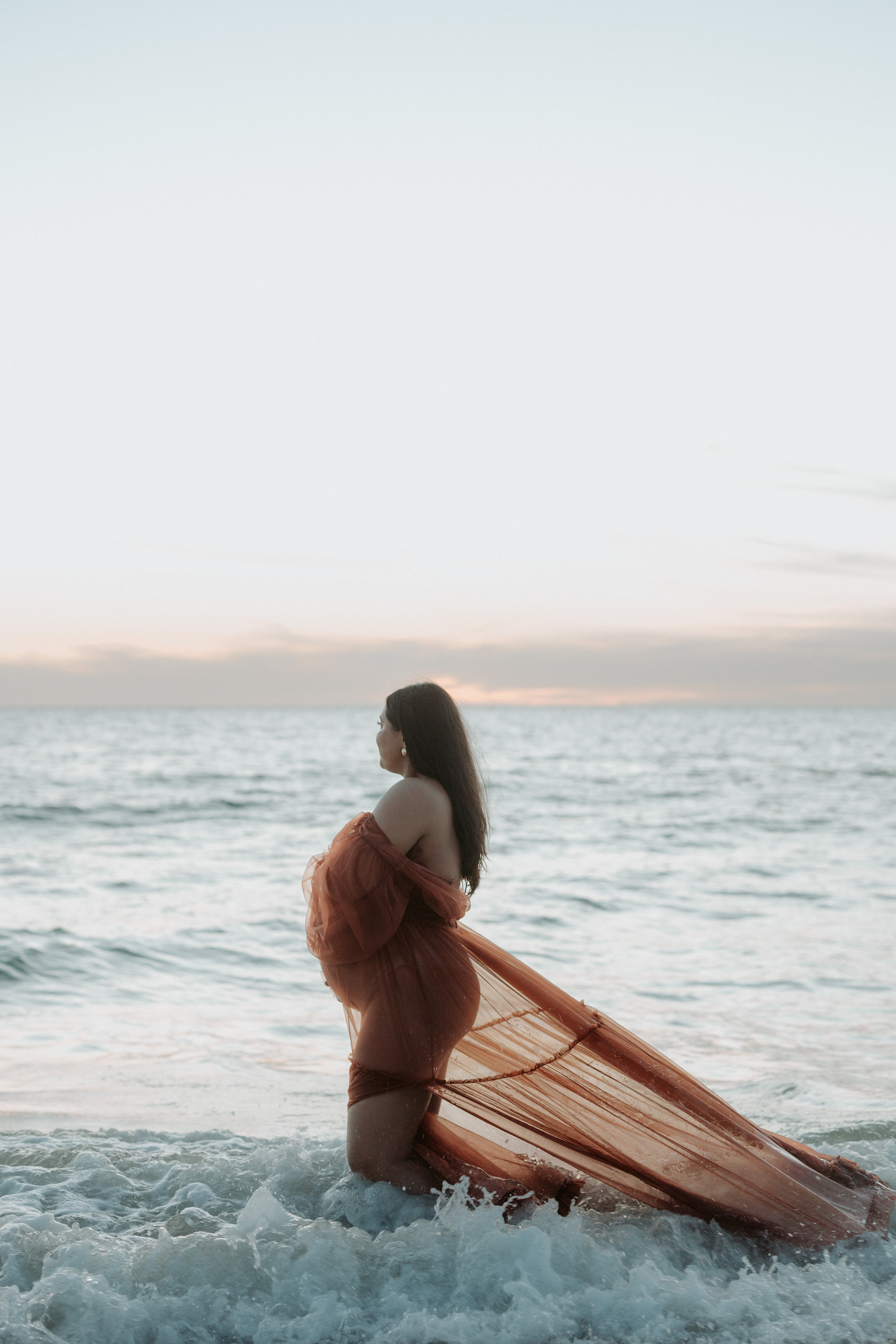 Pregnant woman cradling her belly in a sunlit beach in Perth
