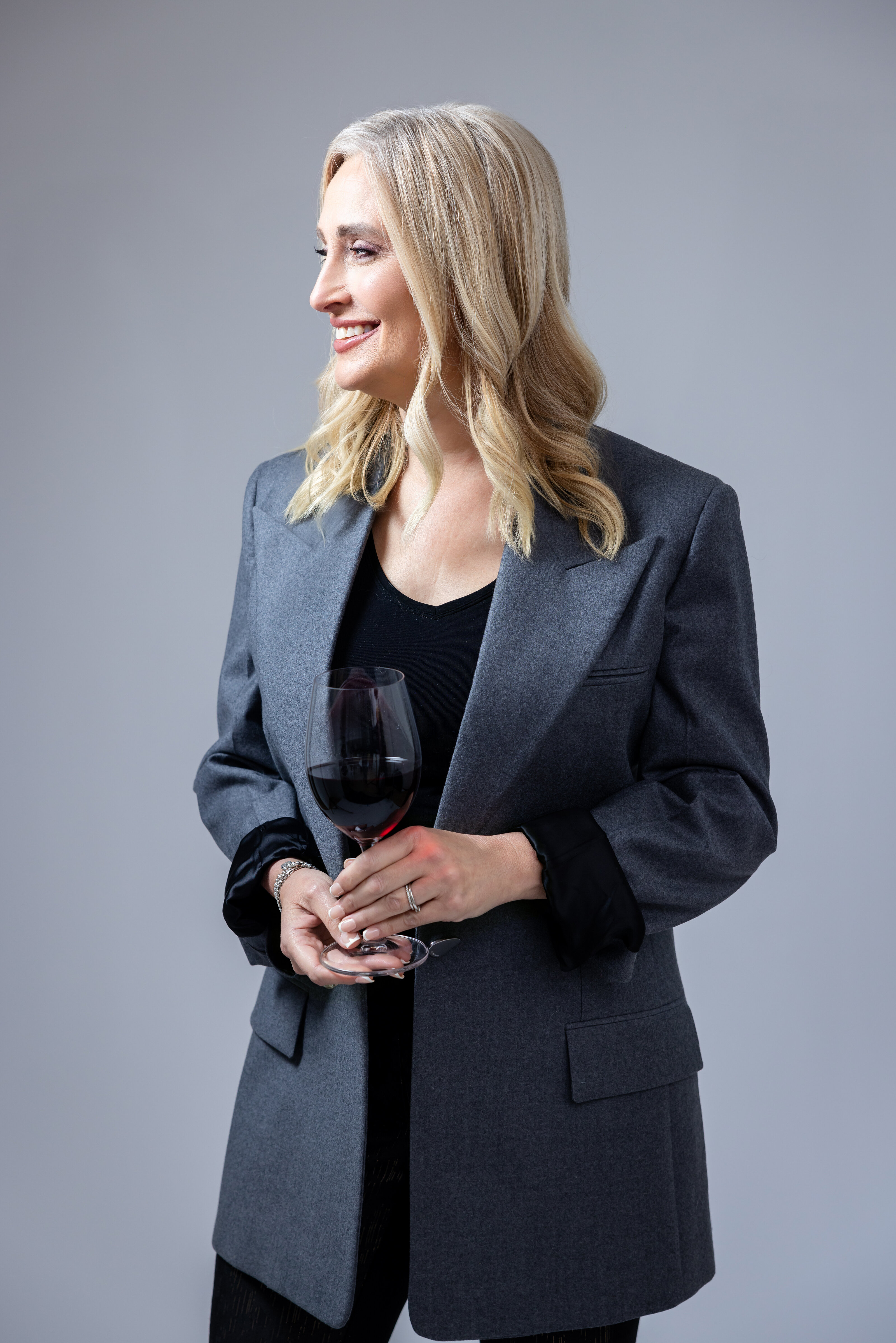 A woman holds a glass of wine while looking away from the camera