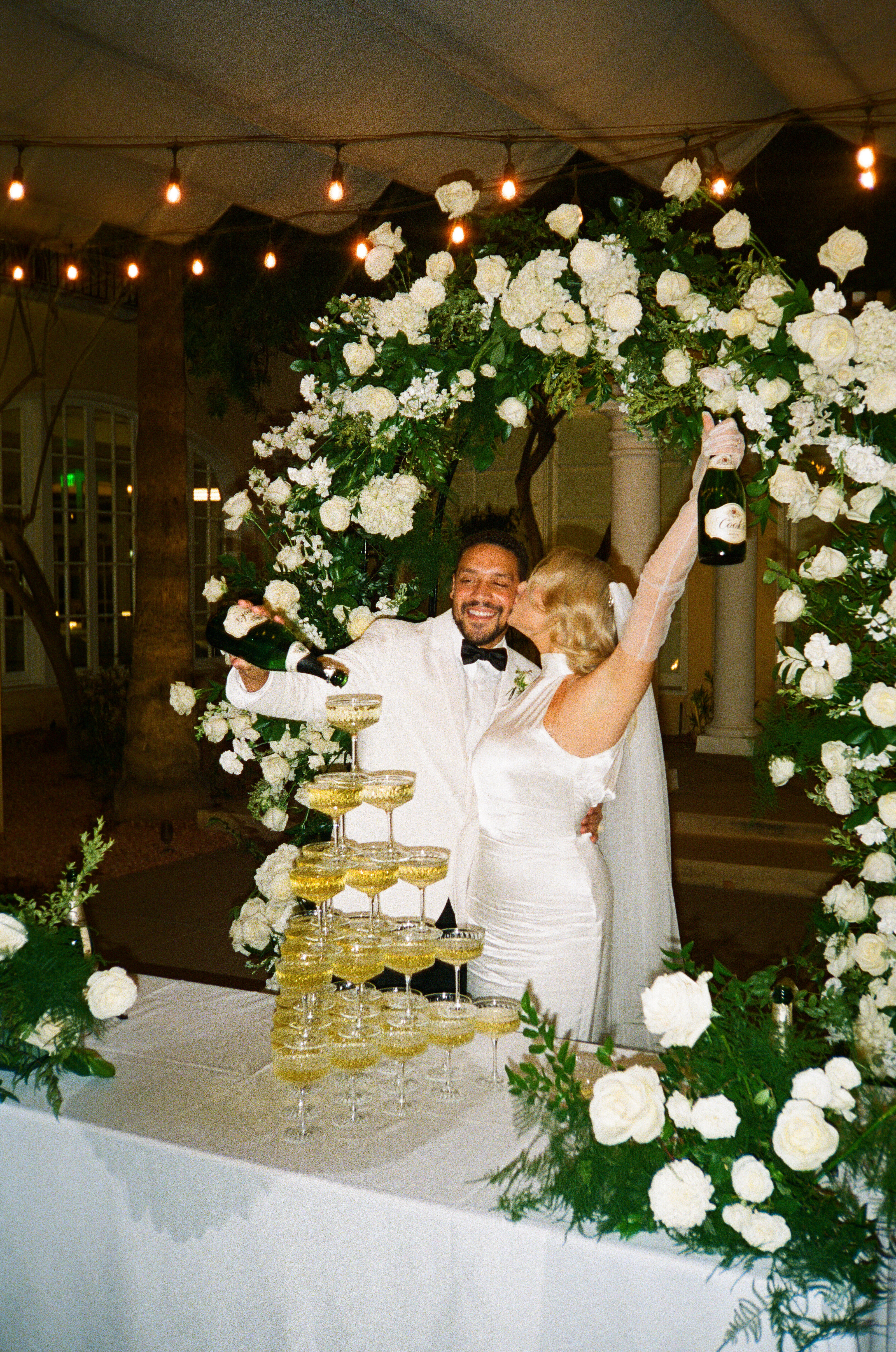 photo of a couple standing behind a champagne tower and kissing while celebrating