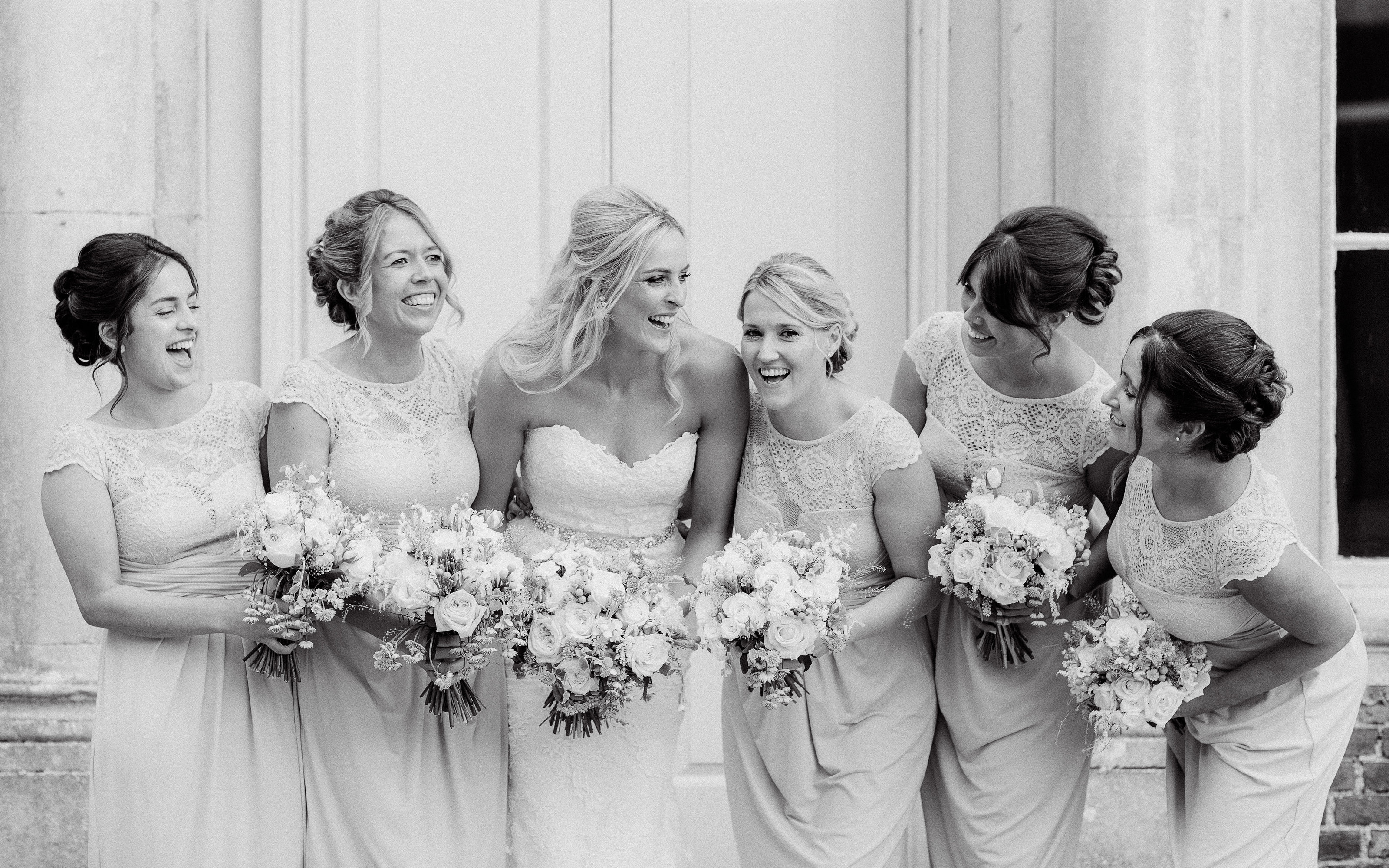 Beautiful bridal party looking at each other laughing in this black and white photo taken by Adorlee Photography in Chichester of Bridesmaids gone wild