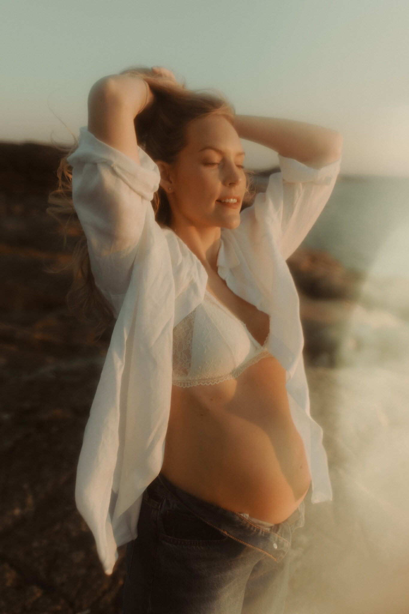 en gravid kvinna lyfter sitt hår och ser avslappnad ut med solens strålar mot henne