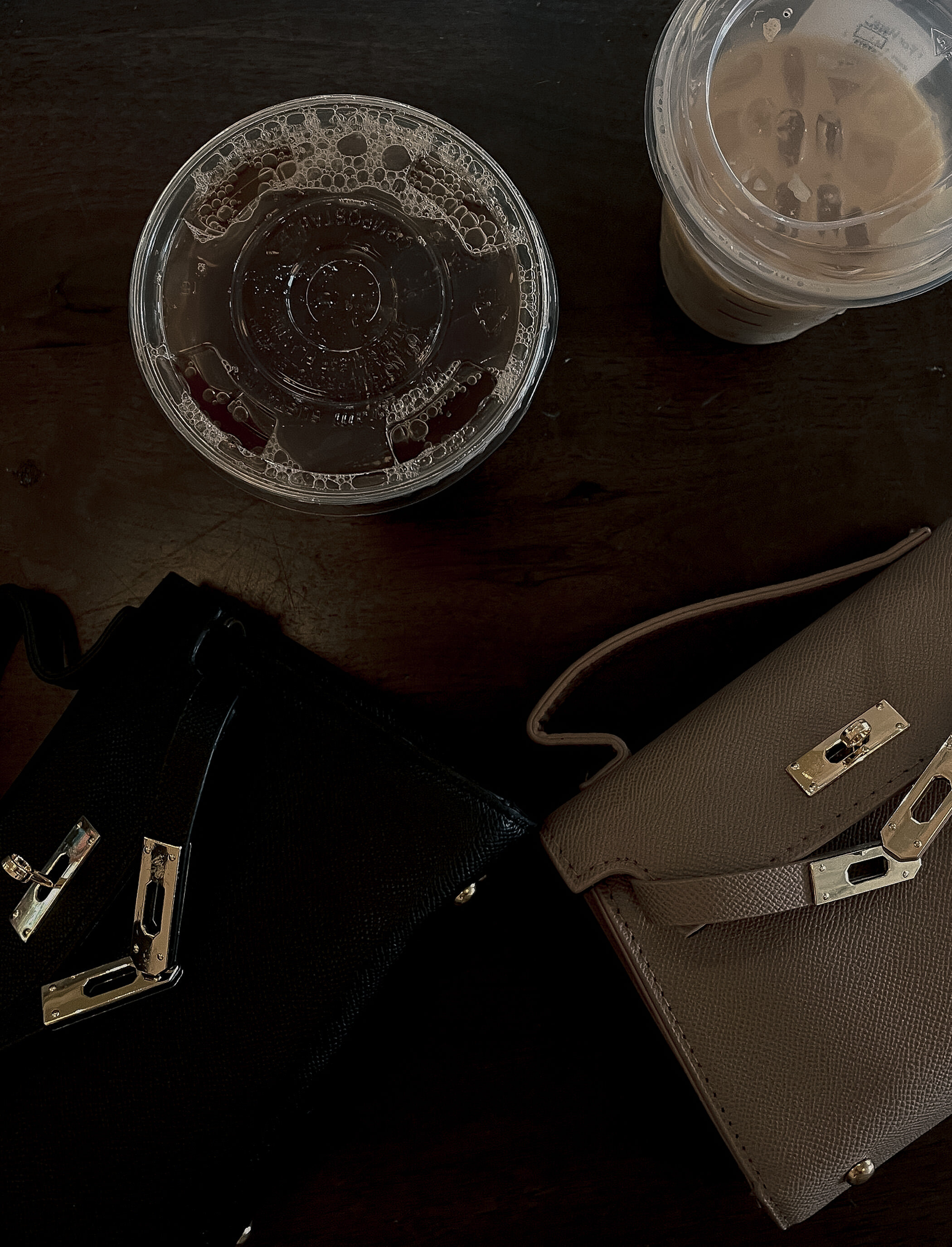 Purses and drinks sitting on a dark wooden table