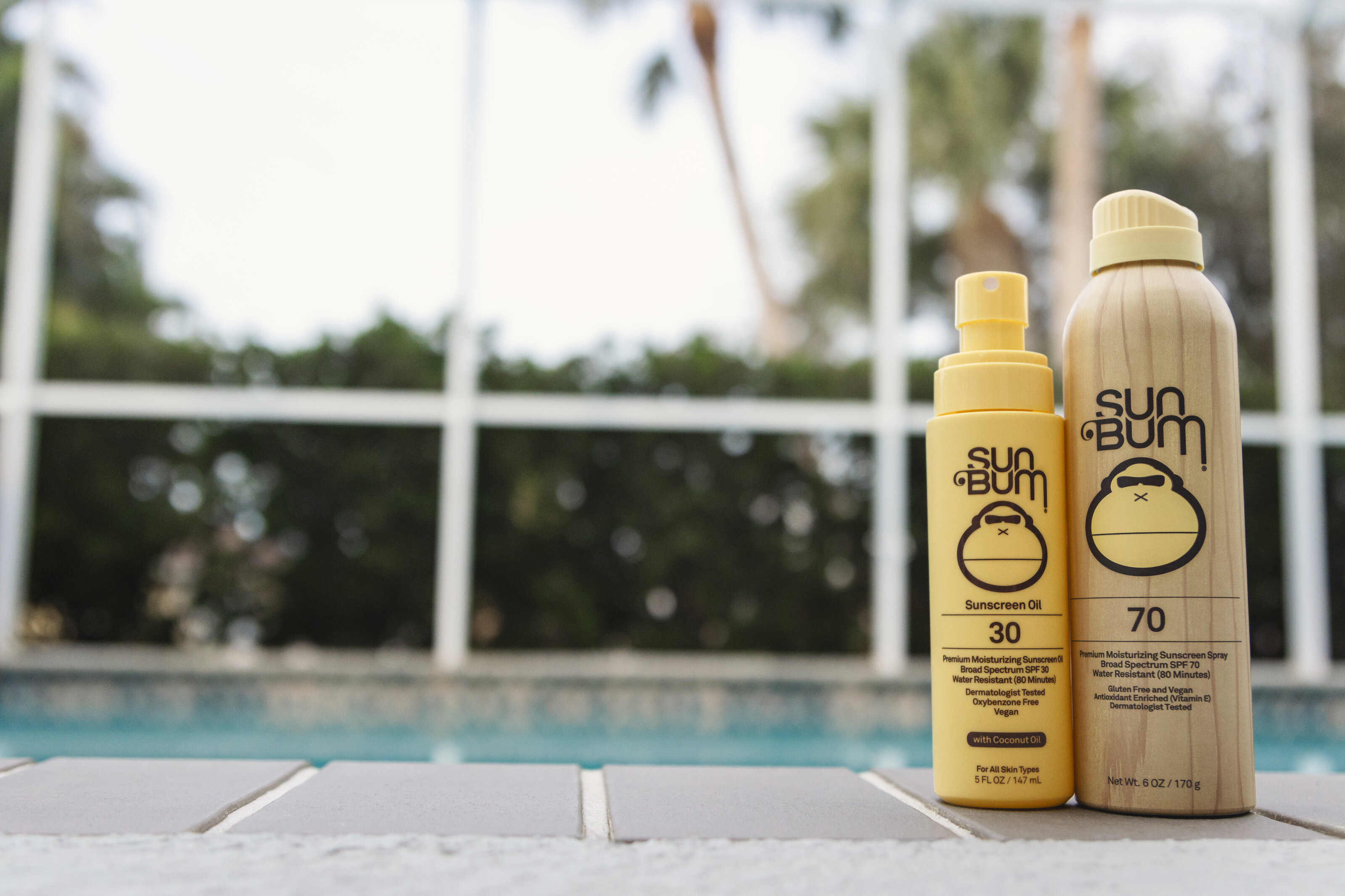 SunBum products photographed beside a pool with palm trees in the background