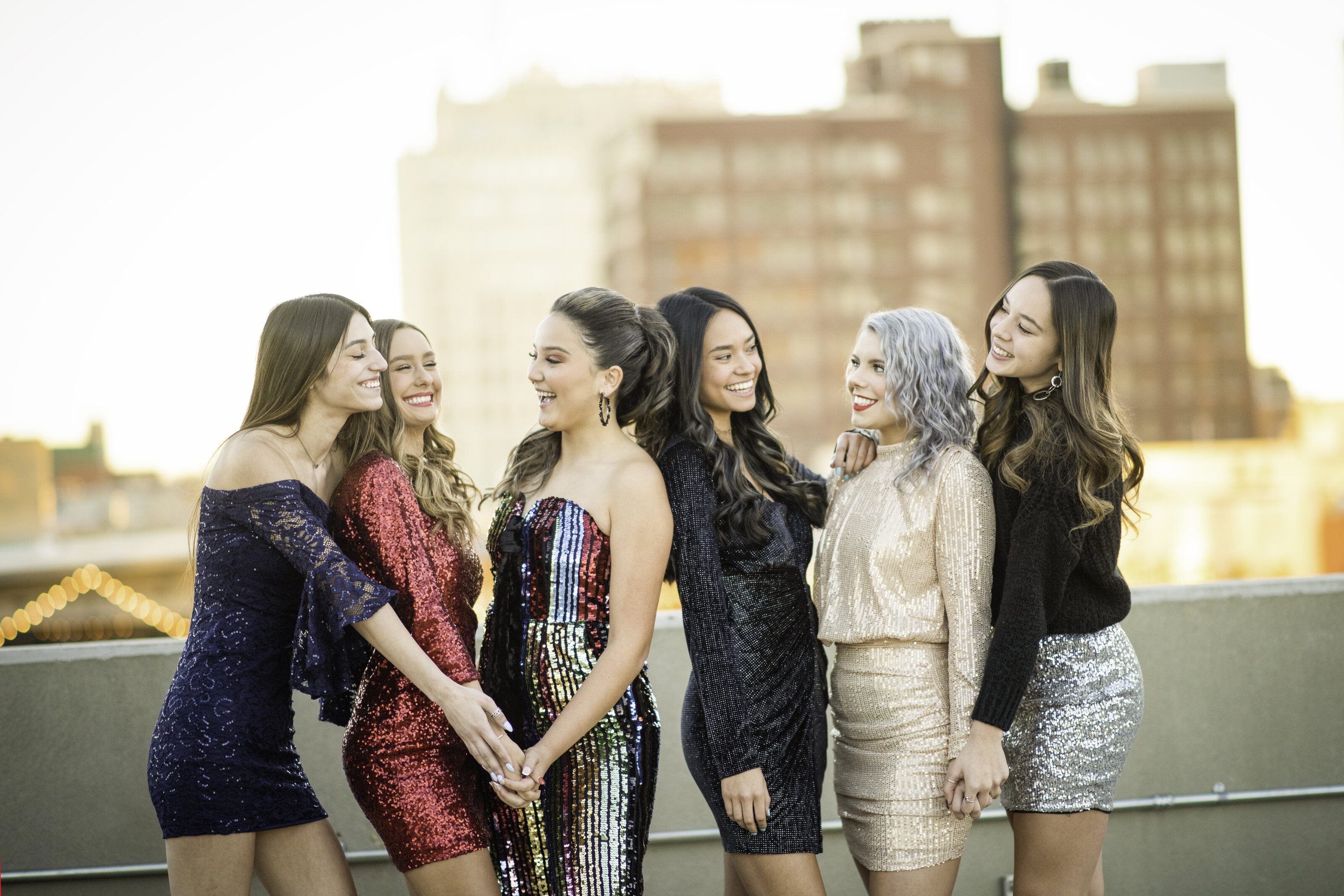 A group of high school seniors in sparkly outfits takes pictures on top of a parking garage downtown Amarillo.