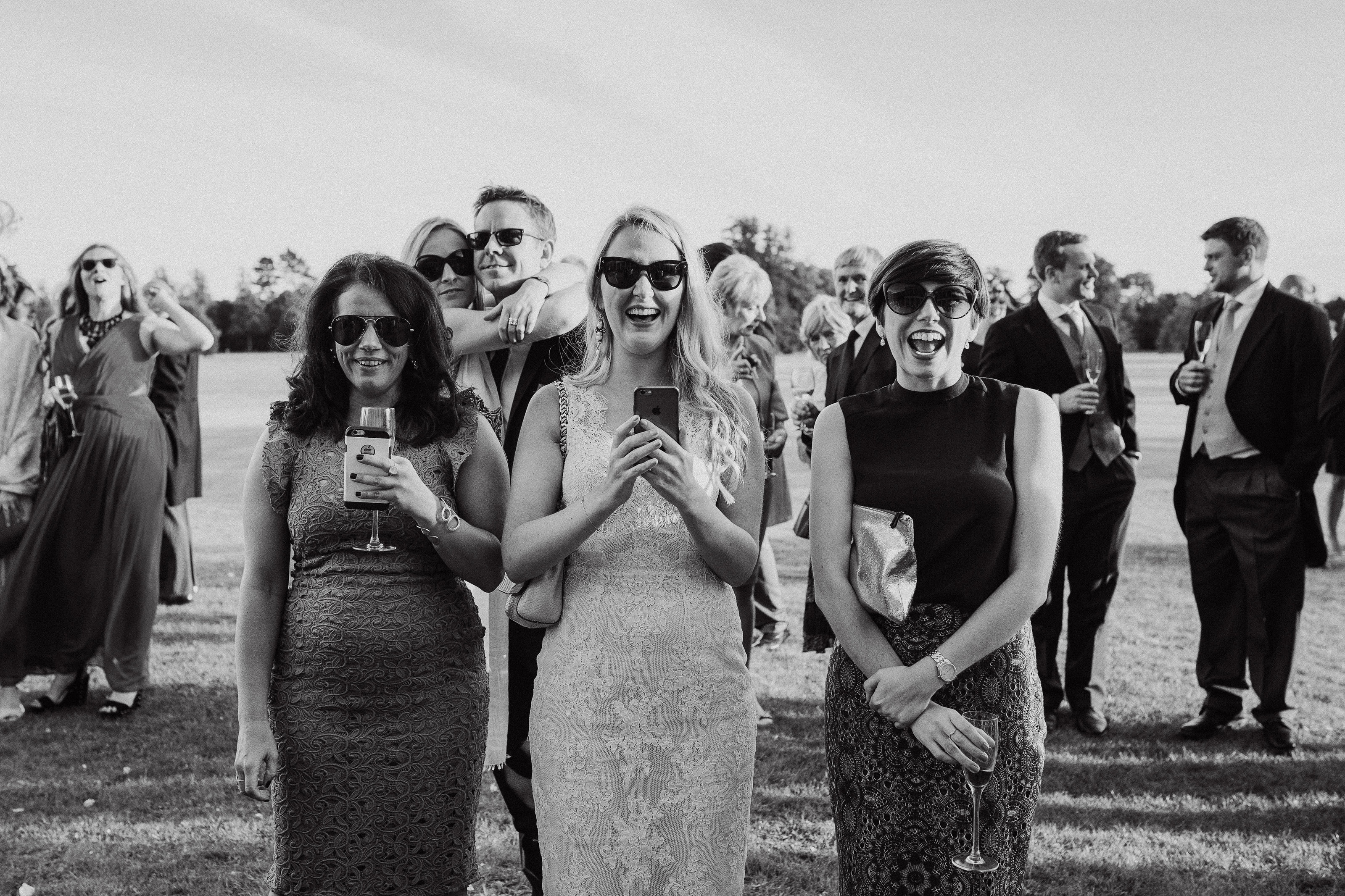 Three guests laugh in this candid black and white moment captured by Adorlee Photography at Goodwood House in Chichester