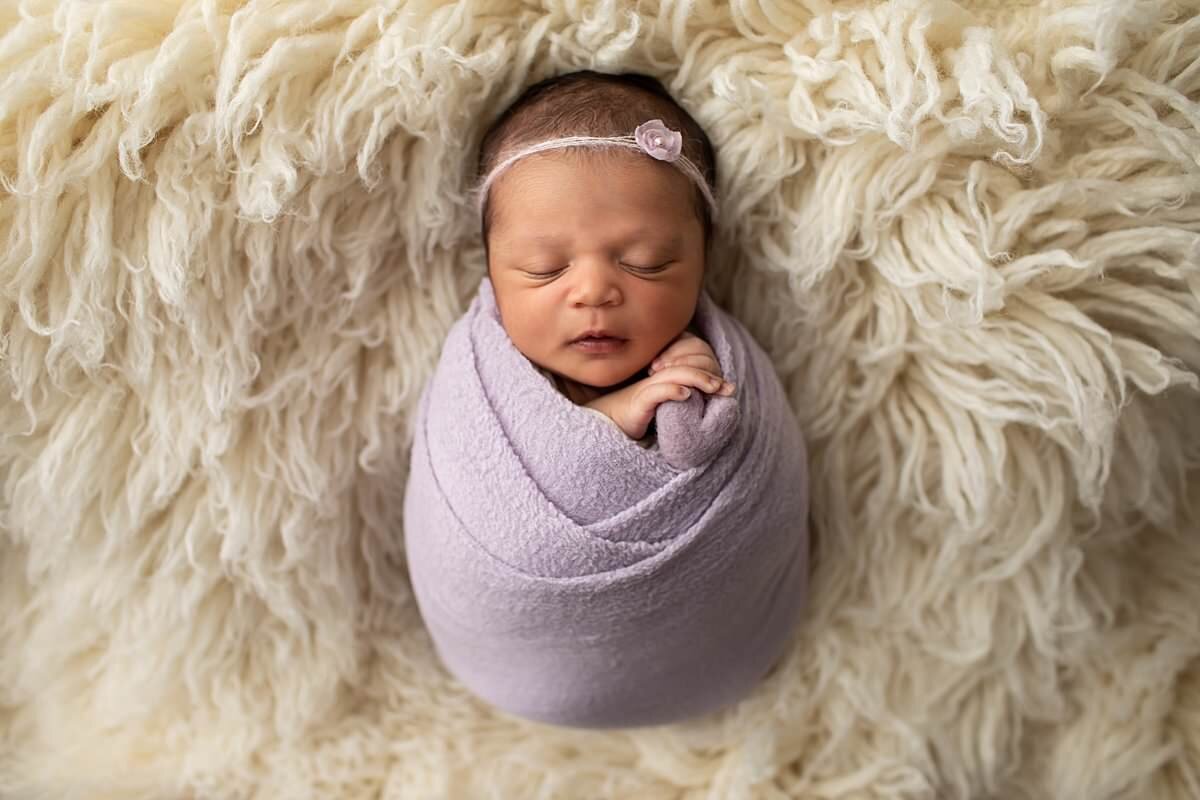 Baby wrapped in purple swaddle on furry blanket for newborn photos in Columbia MD