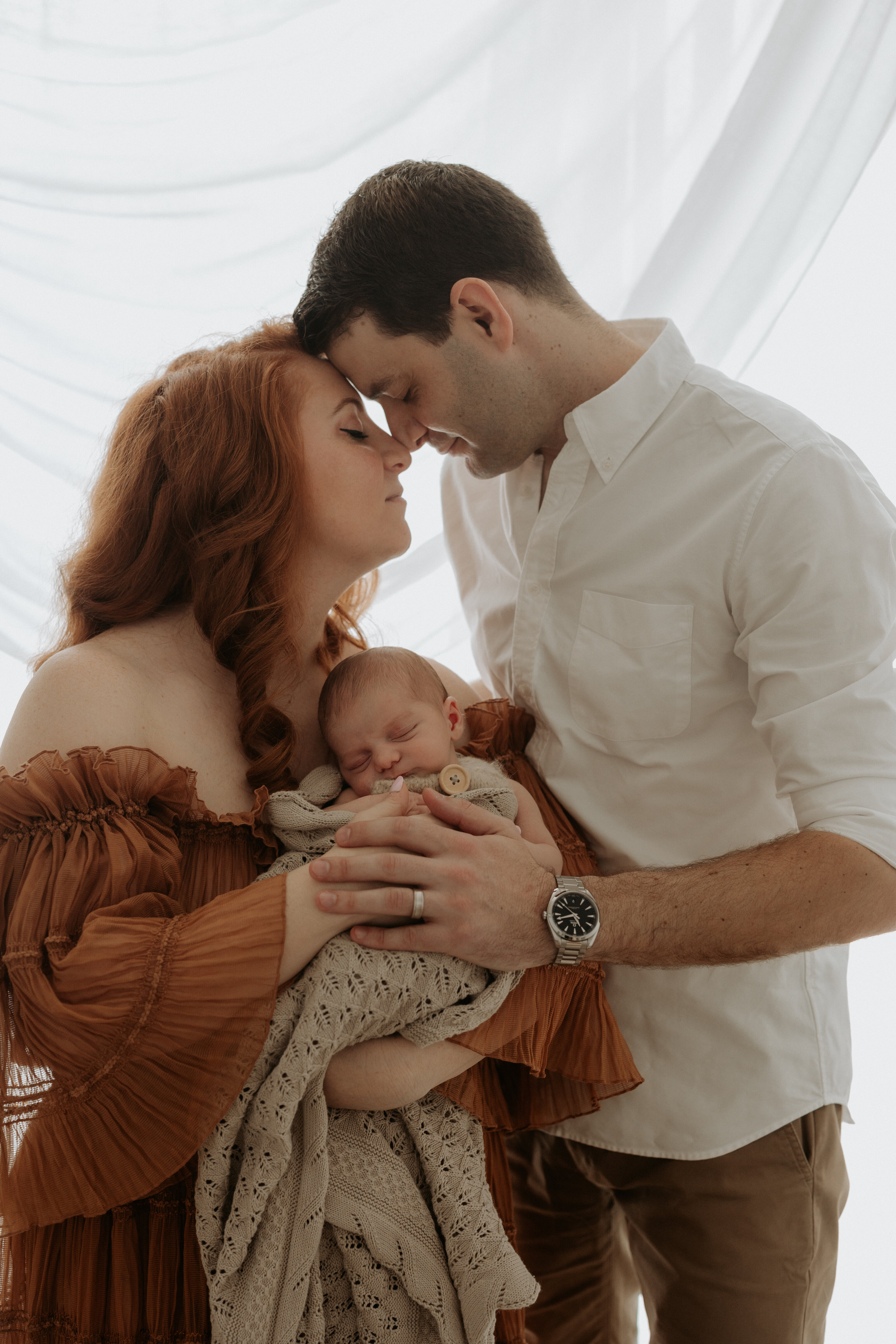 Tender family cuddle with their newborn in a warm indoor setting in Perth