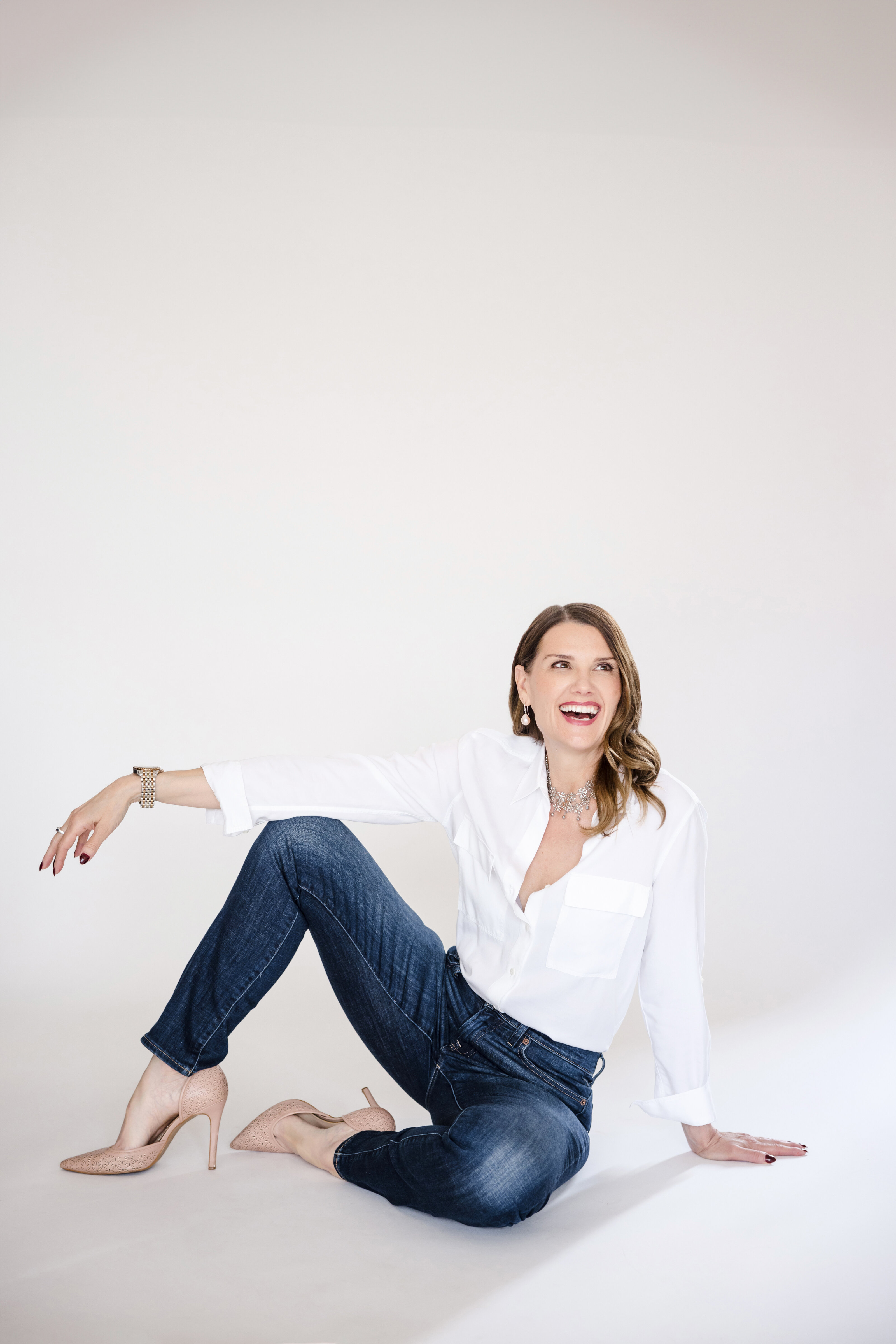 A woman in a white shirt sits on the ground while laughing