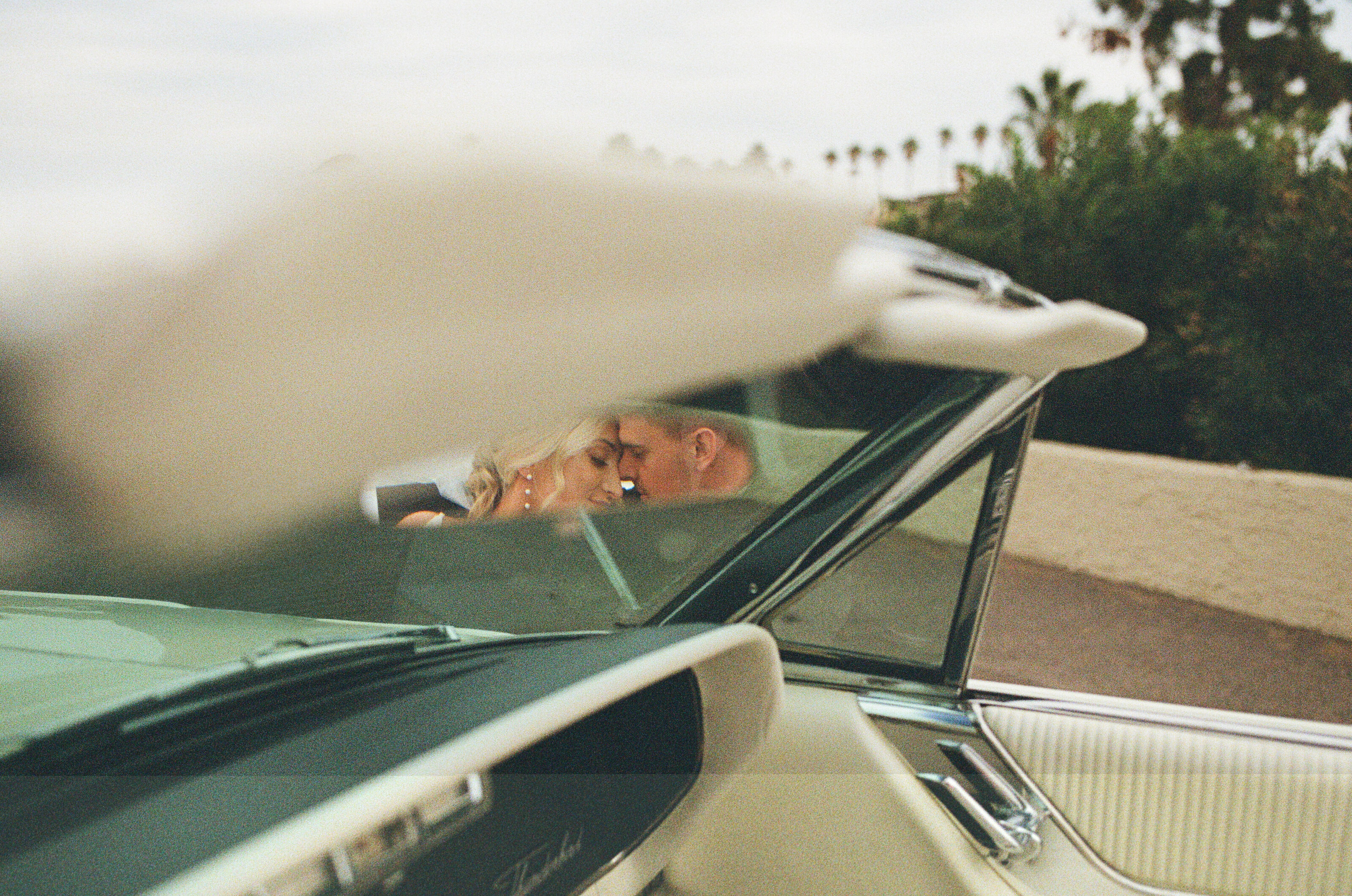 photo of a couple looking at eachother through a vintage car's rear view mirror