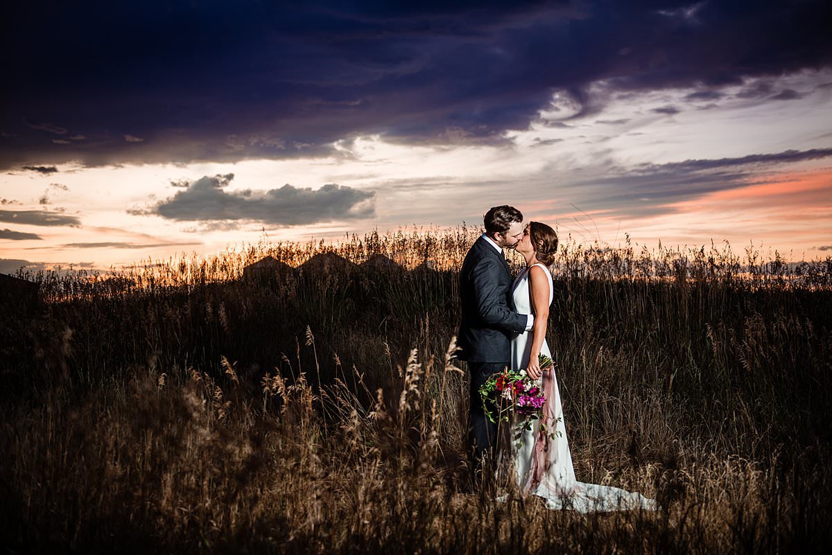 Bride and Groom kissing in a field during a purple and peach sunset in Montana