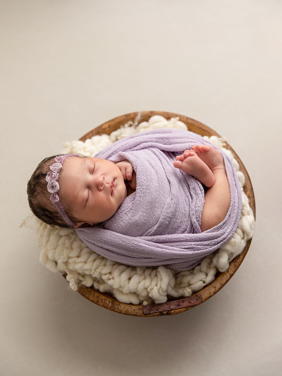Sleeping baby girl in purple wrap in wooden bowl by Columbia MD newborn photographer