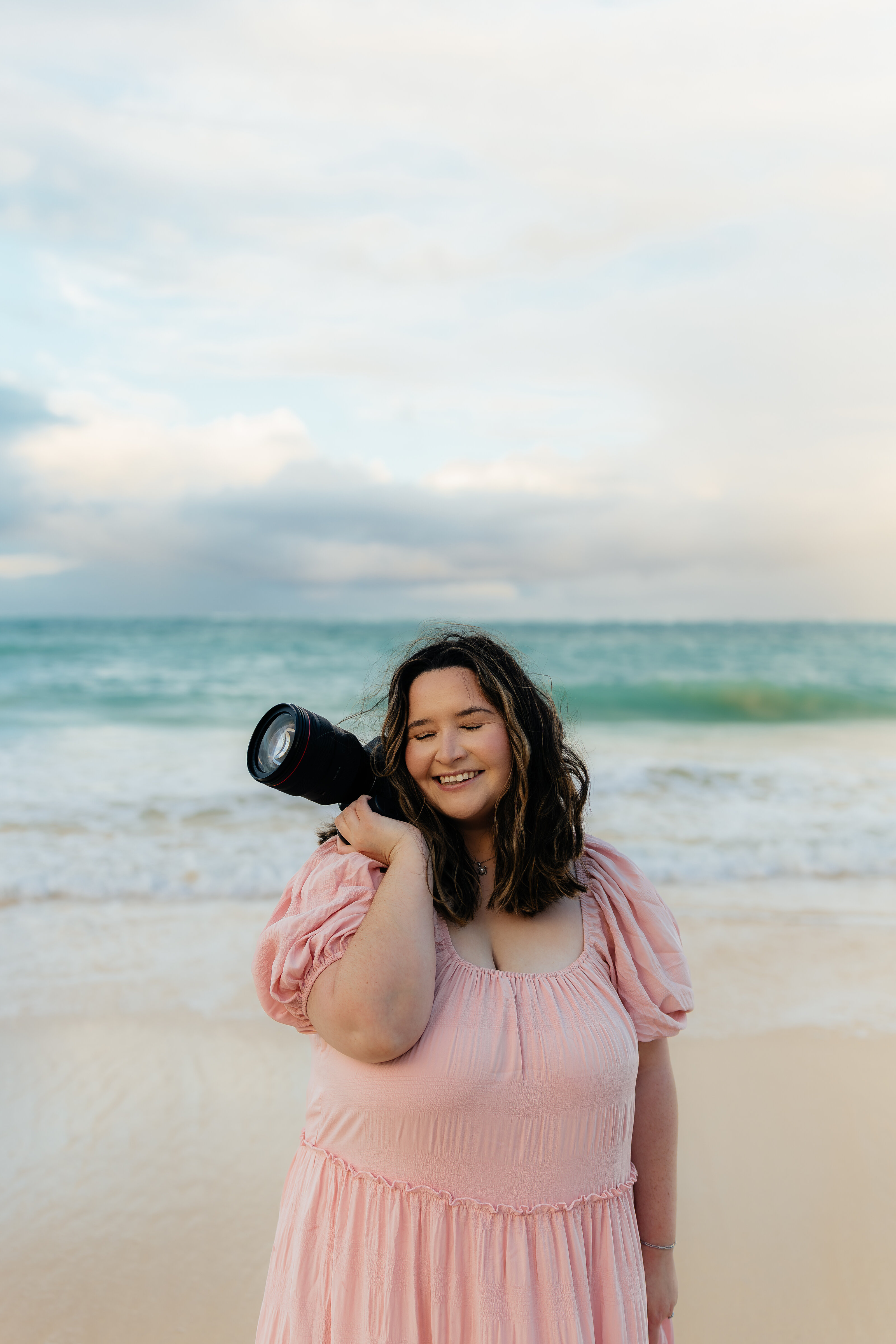 Lexi, an Hawaii photographer, in a pink dress on the beach with her camera