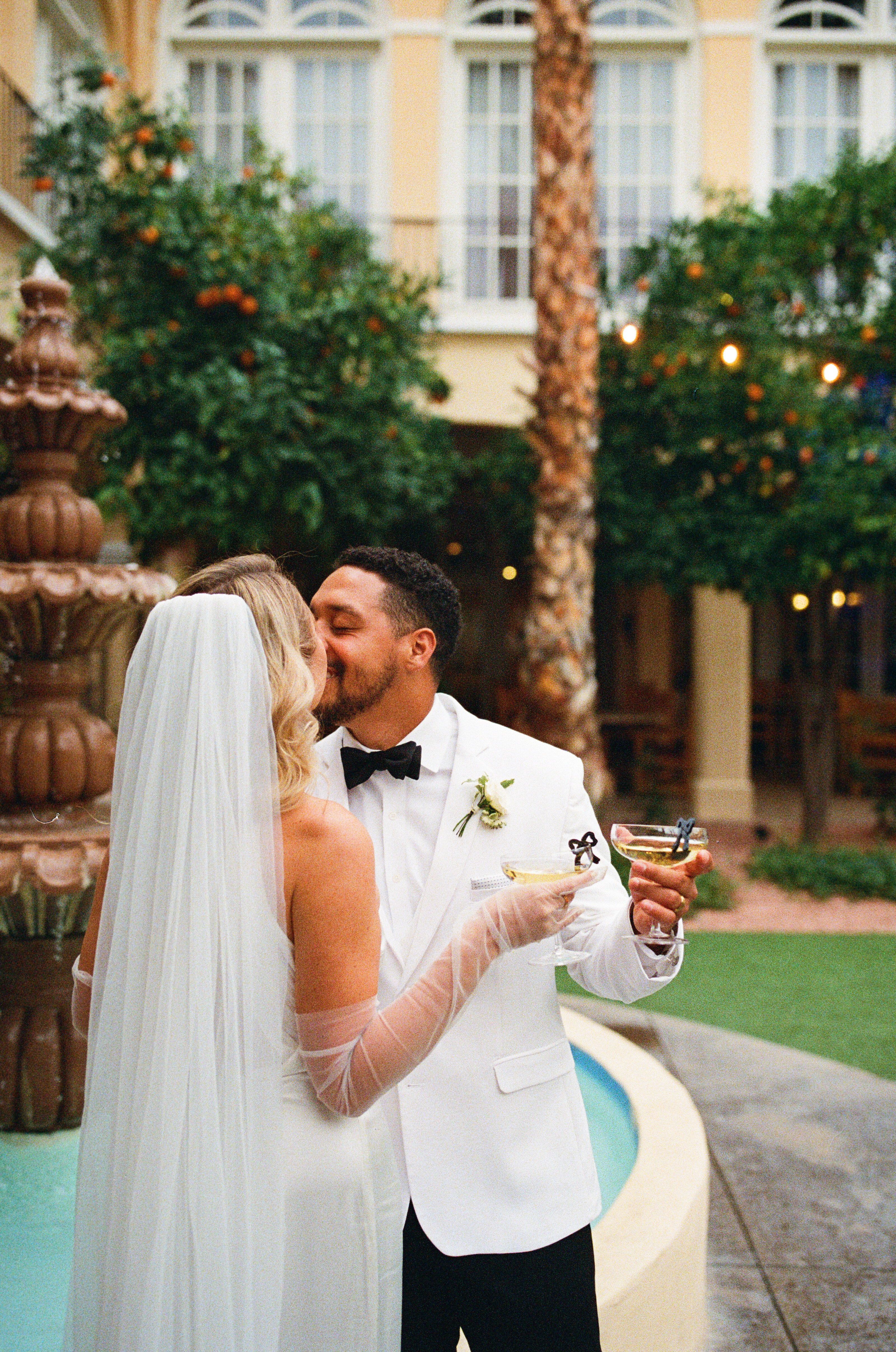 a couple hugging and kissing in front of a fountain at chandler san marcos crowne plaza resort while drinking champagne