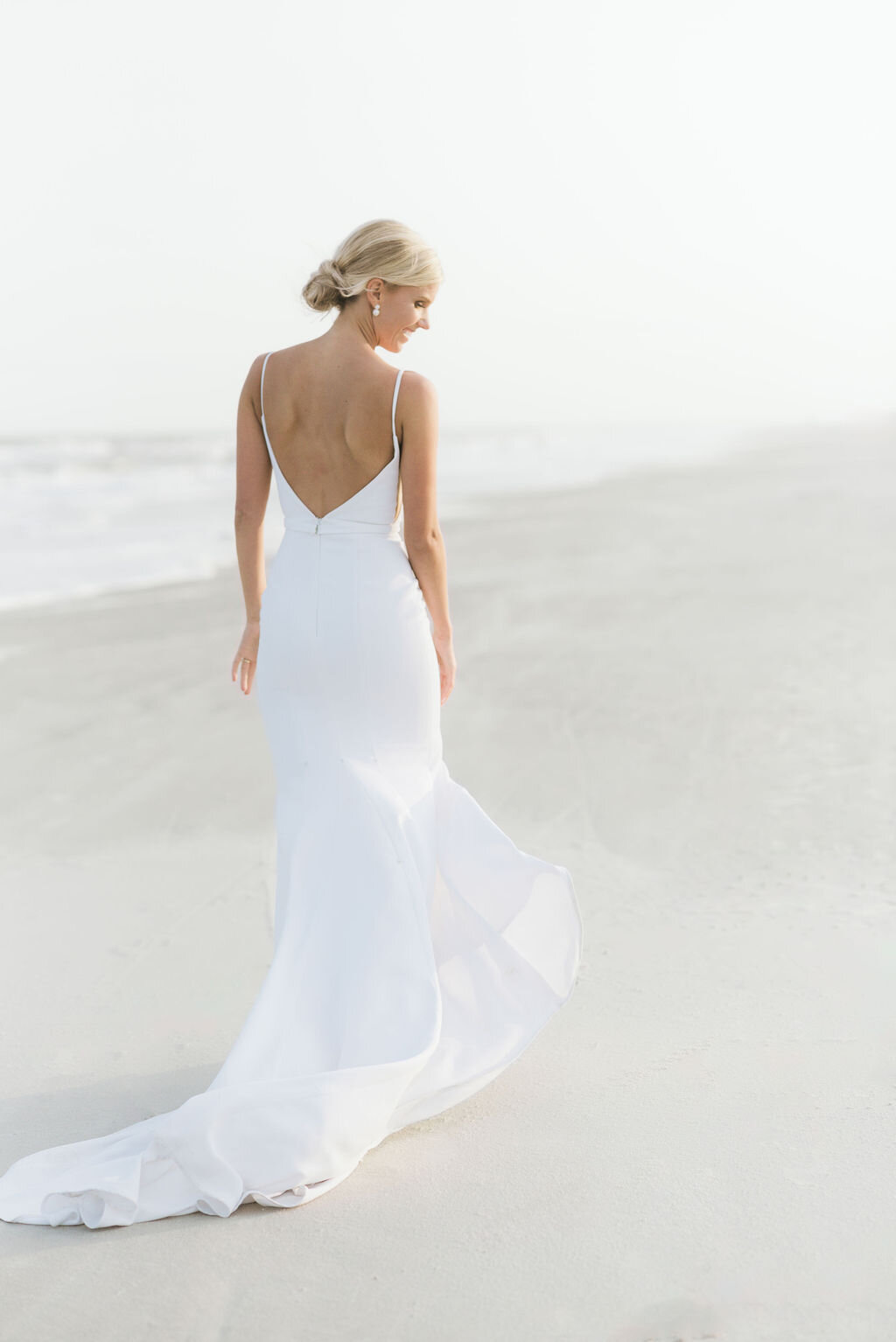 A stunning bride walks along the shoreline in a flowing white gown during her luxury beach wedding at Hilton Head Island. A serene and timeless bridal portrait.