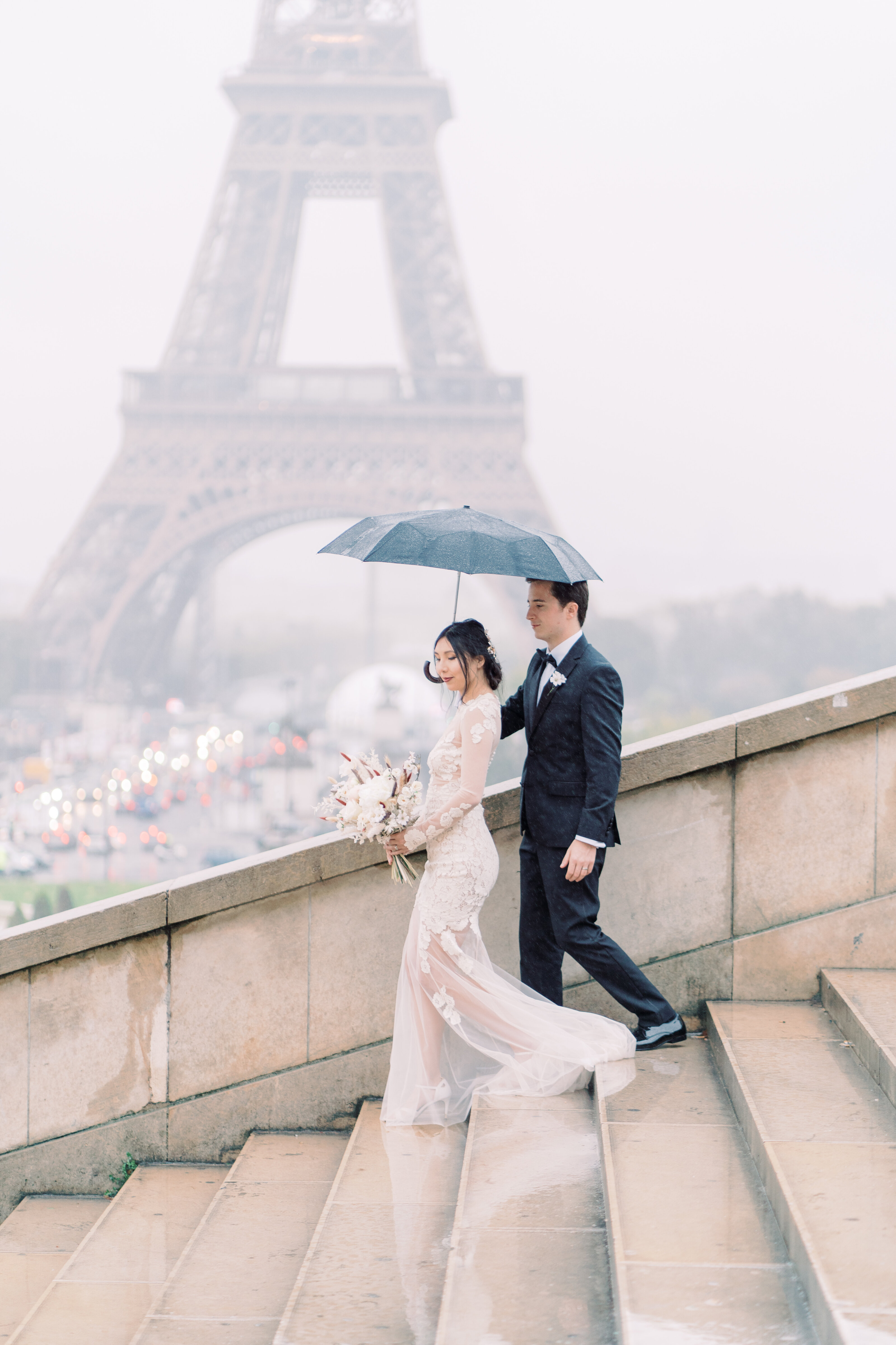 Bride and groom walking under an umbrella near Eiffel Tower in Paris.