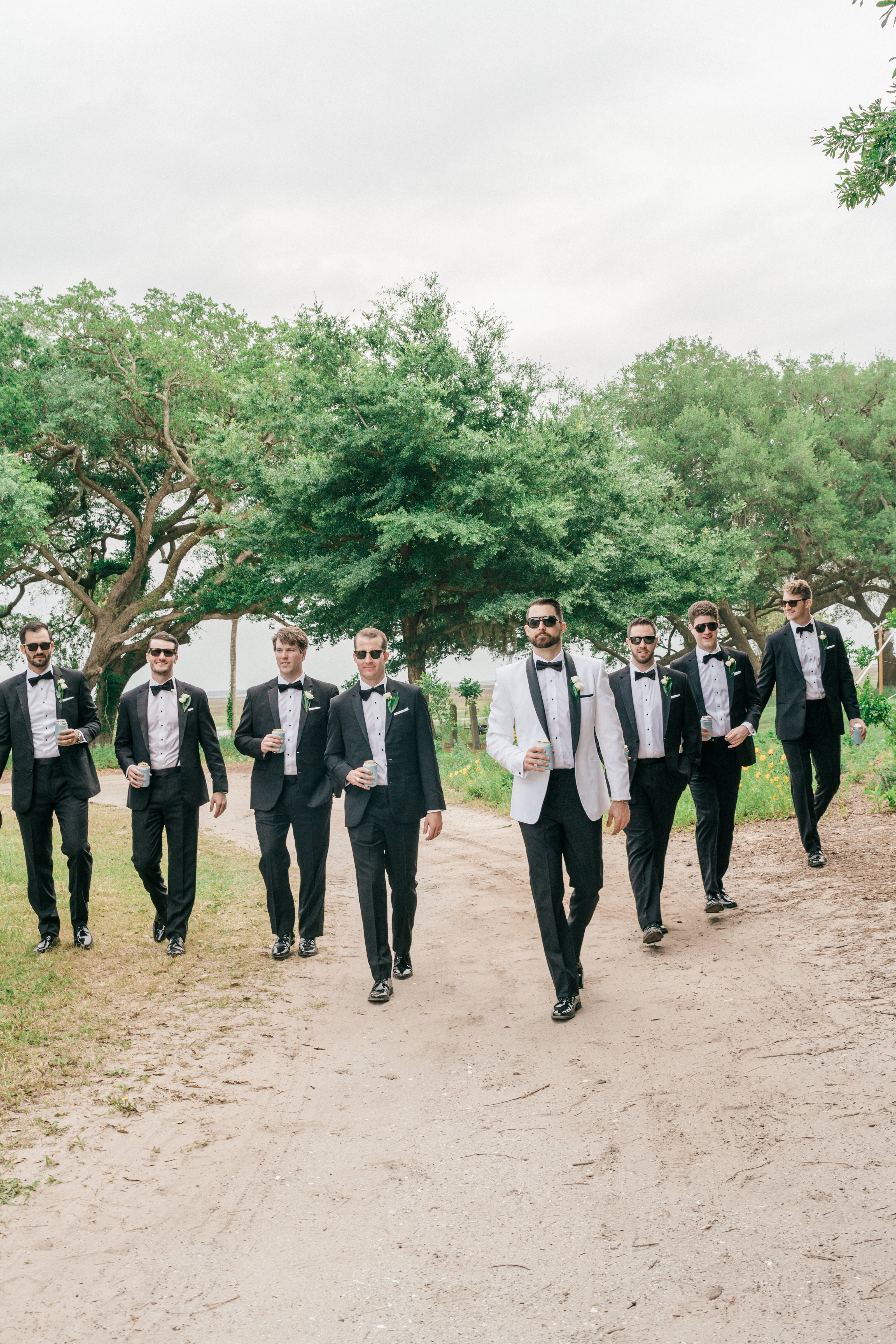 A stylish groom in a white tuxedo leads his groomsmen in black-tie attire at a luxury Spring Island, SC wedding. A refined and modern wedding party portrait.