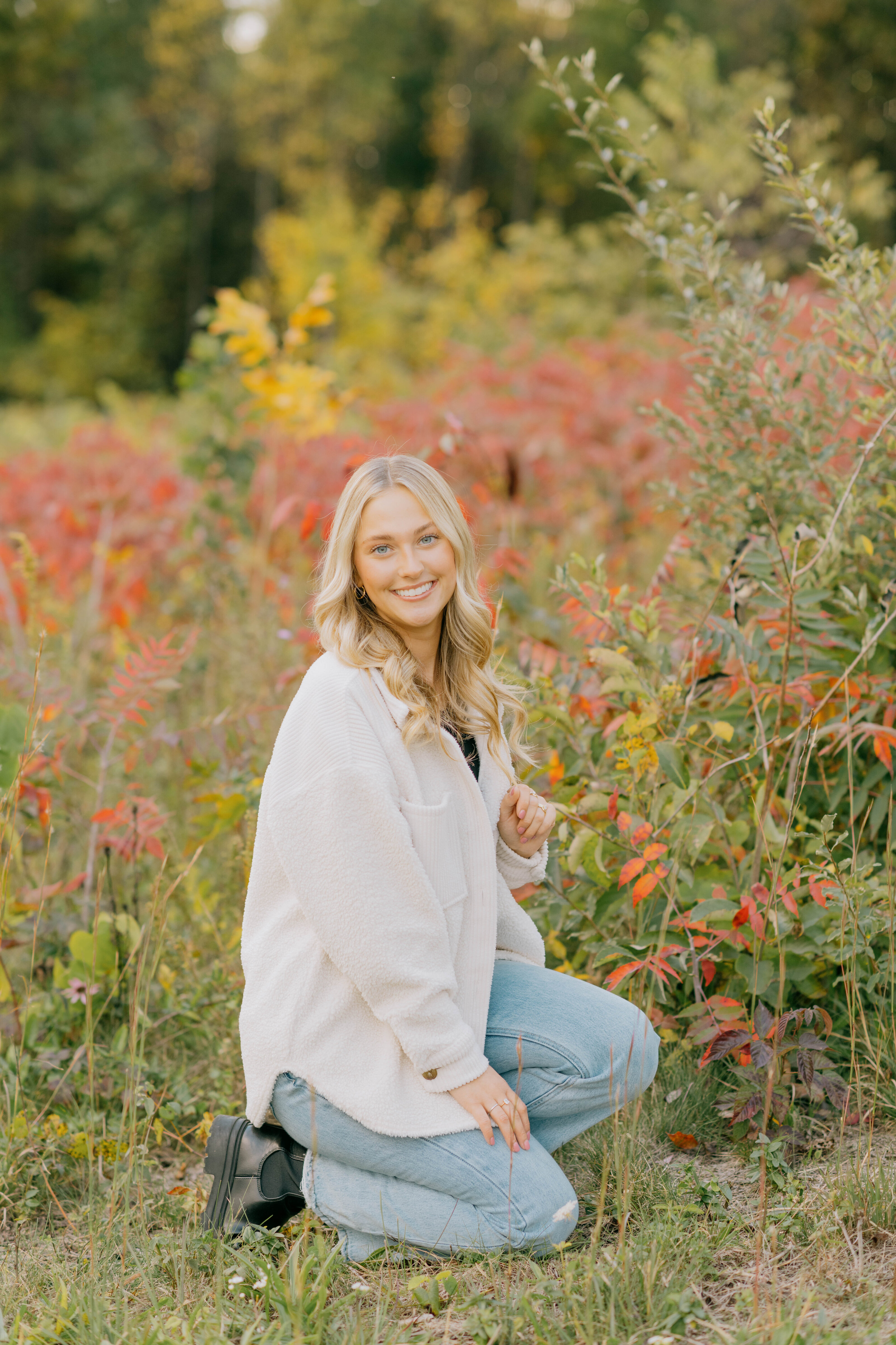 Corrin crouches in a field of vibrant foliage near Harrisonburg for her fall senior portraits.