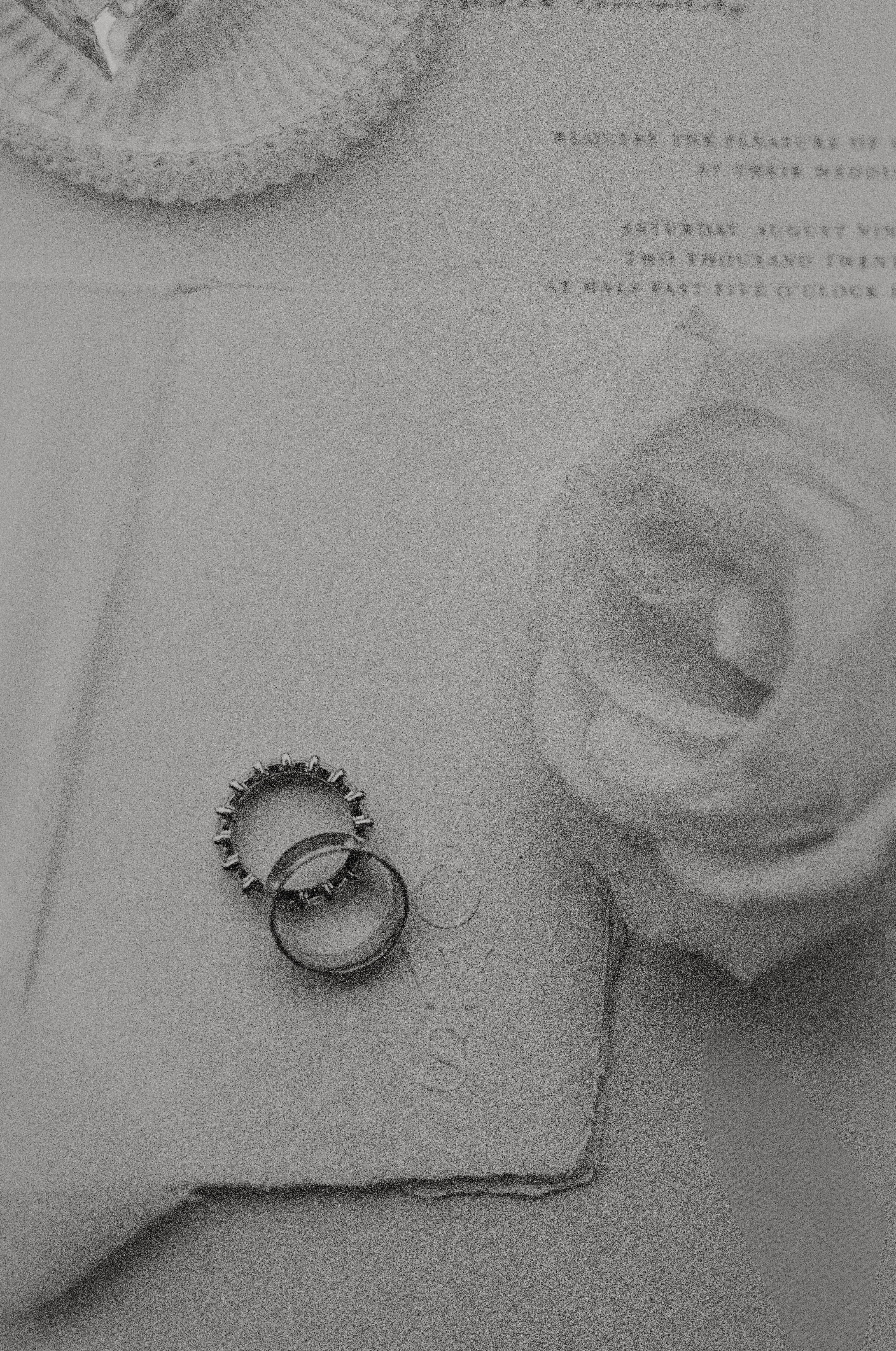 black and white photo of  vow books sitting on a table with wedding rings stacked on top of them