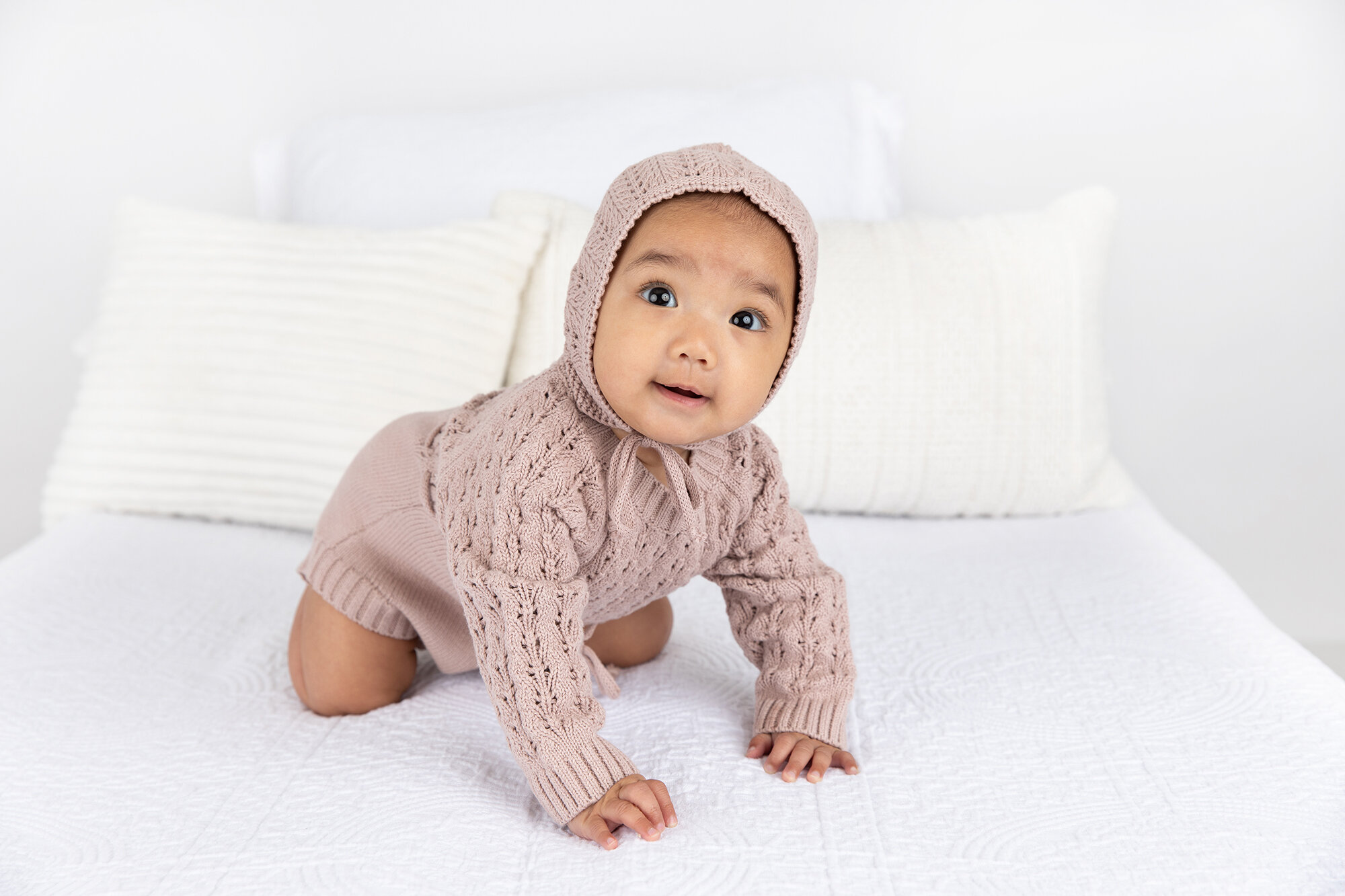 baby girl in a mauve knit outfit and bonnet crawling