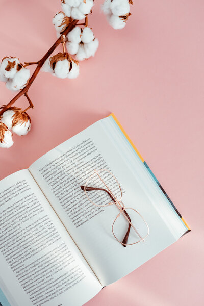 kaboompics_an-open-book-glasses-and-a-cotton-branch-on-a-pink-background-9158