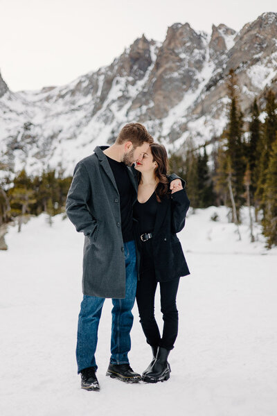 Couple with foreheads gently touching, his arm wrapped around her, as they enjoy the stunning view of Dream Lake in Rocky Mountain National Park, Estes Park, during their engagement session.
