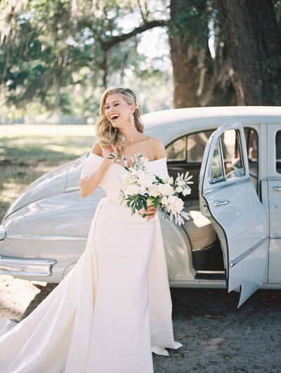 Bride laughs and holds her bouquet under a tree at her Middleton Place Wedding in Charleston South Carolina