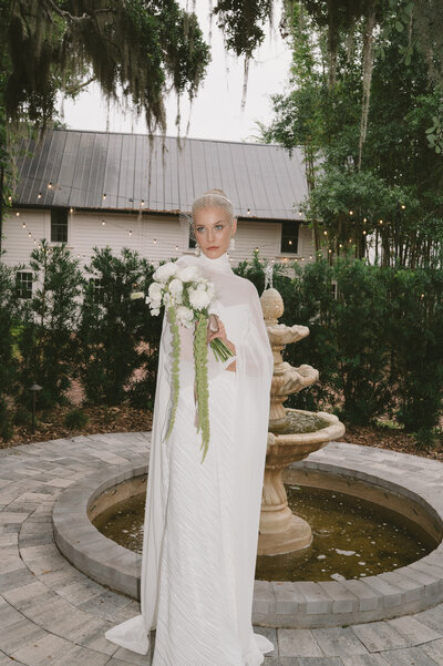 Hair and Makeup Orlando Florida | Luxury Bridal Hair and Makeup Services in Central Florida Beauty Brigade | Bride in soft glam makeup holding a champagne bottle standing beside the wedding cake