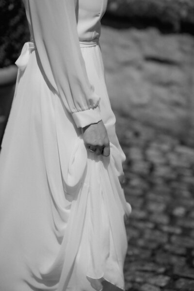 Eine Nahaufnahme der Braut, wie sie ihr Kleid mit einer Hand hochrafft.