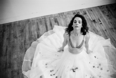 Bridal Boudoir photography of bride resting on ground with flowers covering and sprinkled over her dress.