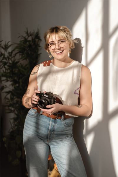 Philadelphia Photographer Heather McBride holding a camera standing against a wall.