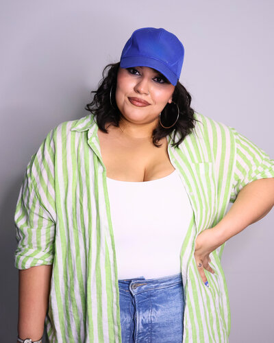 Amanda the Creative Cool Mom Behind Millien Media in a green striped open button down and white tank top with a blue baseball cap.