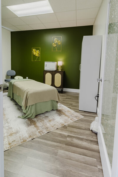 Private massage therapy room with green wall, massage table, and warm lighting