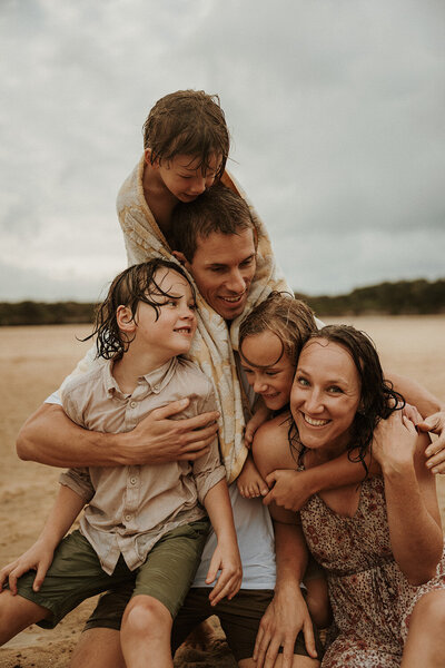 Candid Sunshine Coast family session showing parents and children laughing together on the beach.