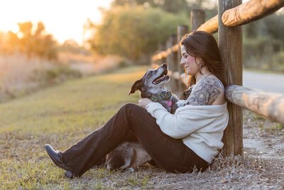 Woman cuddles her senior dog while leaning against a wooden fence