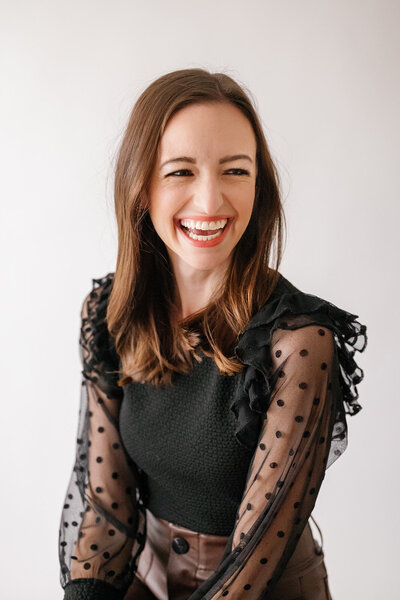 Woman in black top with sheer polka dot sleeves smiling off to the side