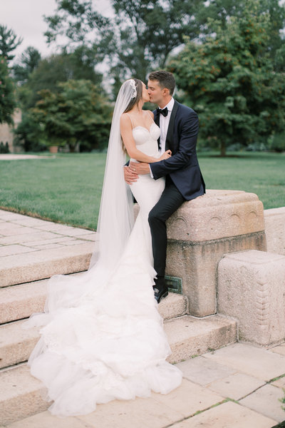 bride and groom sitting together kissing during outdoor Philadelphia wedding