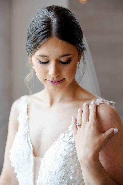bride with hand resting on shoulder showing off her engagement ring while she looks down at it smiling